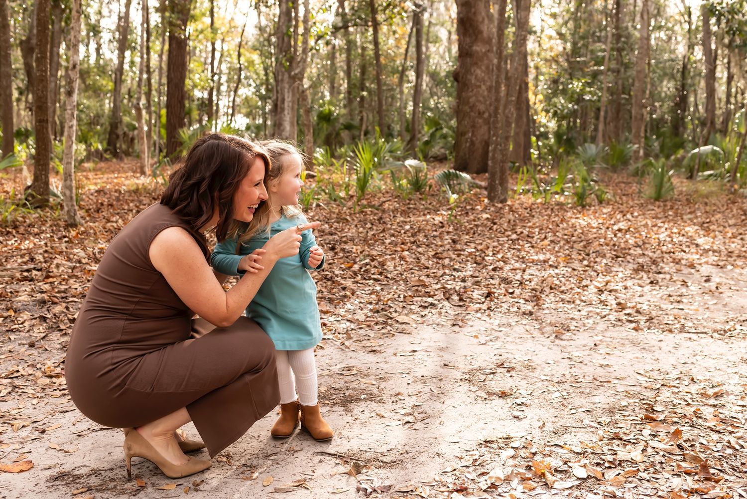 Mother and child share a tender moment on a sunlit dirt path surrounded by autumn trees.