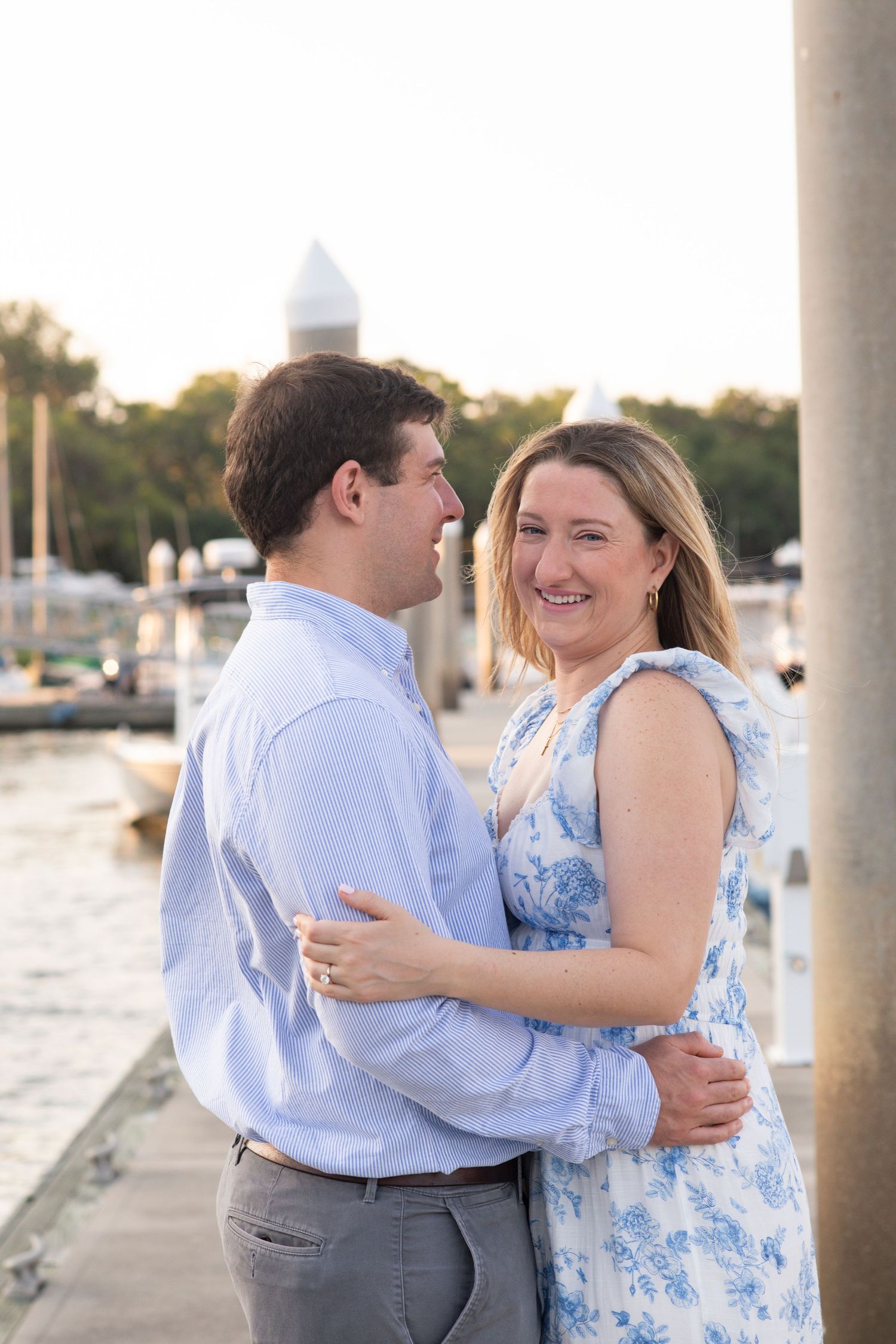 A couple in blue and white attire share joyful moments together during a sunset photoshoot by white columns.