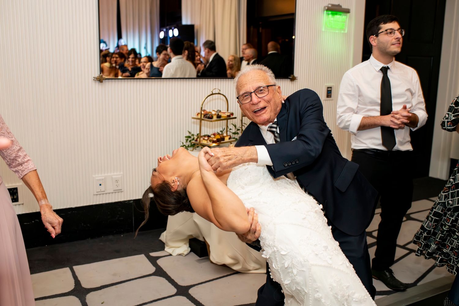 Wedding guests share a playful moment during the reception as a person in a white wedding dress leans back dramatically.