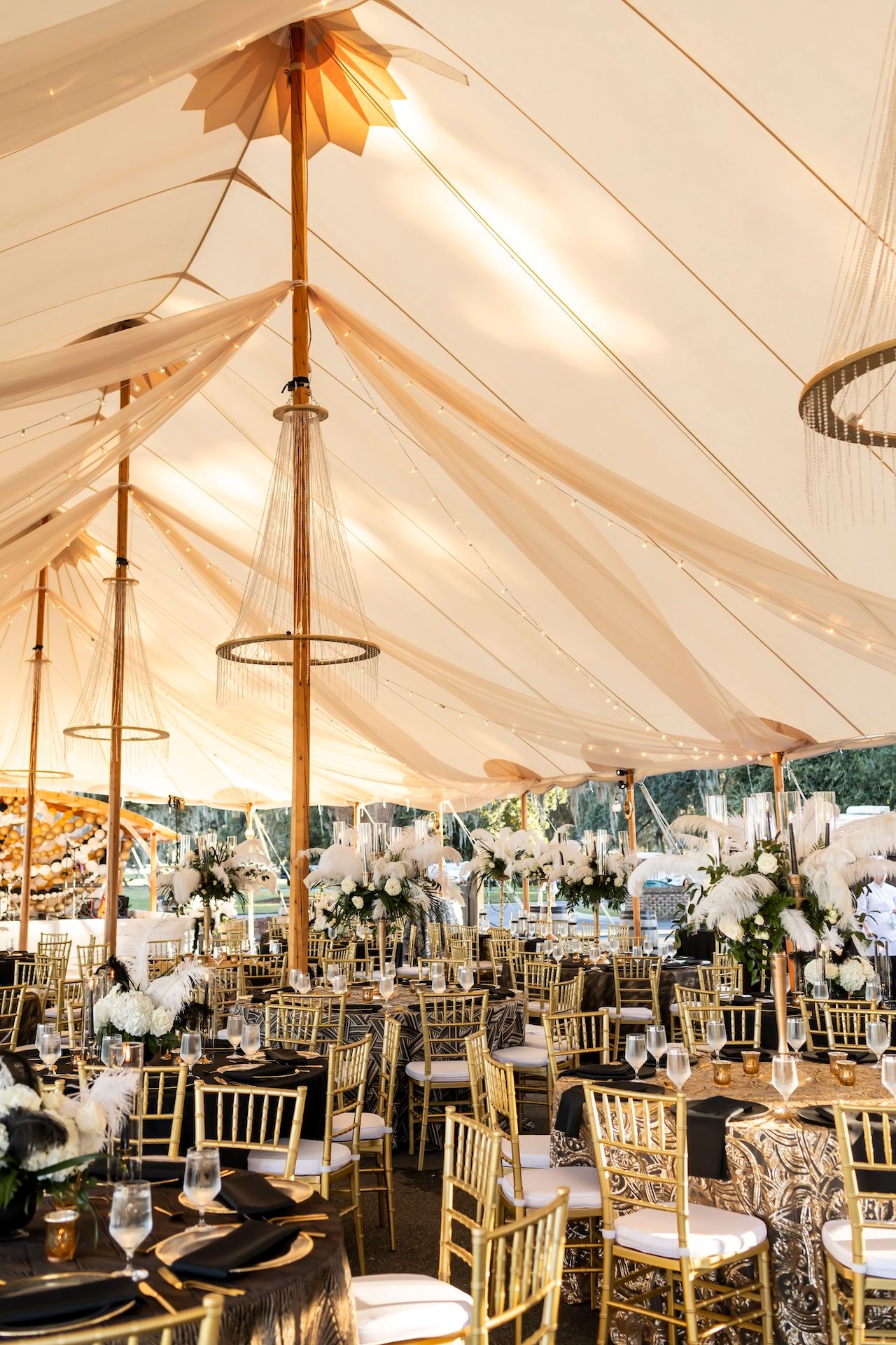 Light beige fabric drapes create an elegant tented ceiling with gold chandeliers and chiavari chairs in a luxurious reception setup.