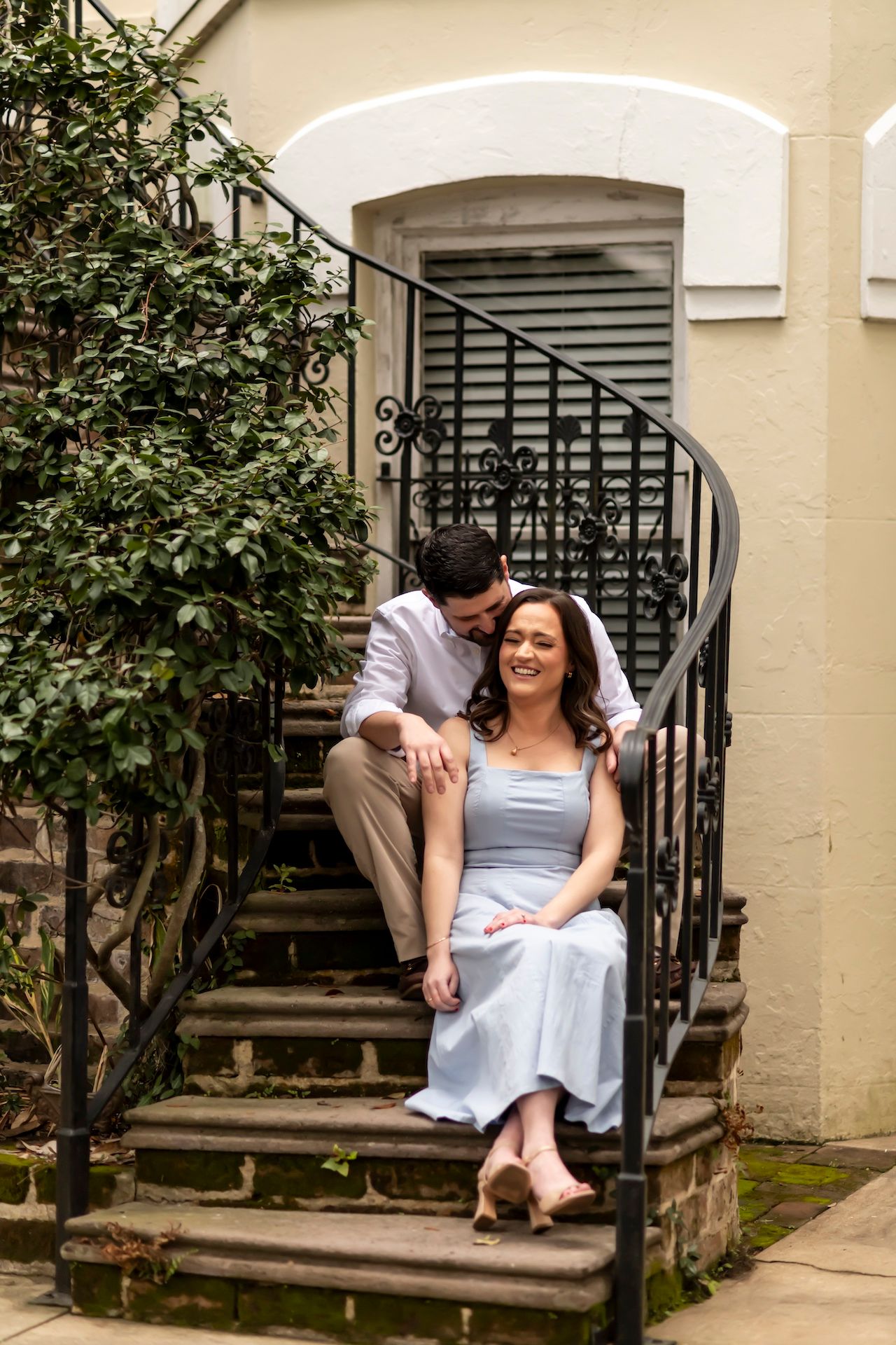 A couple sits together on charming outdoor stone steps with an ornate wrought iron railing and arched doorway.