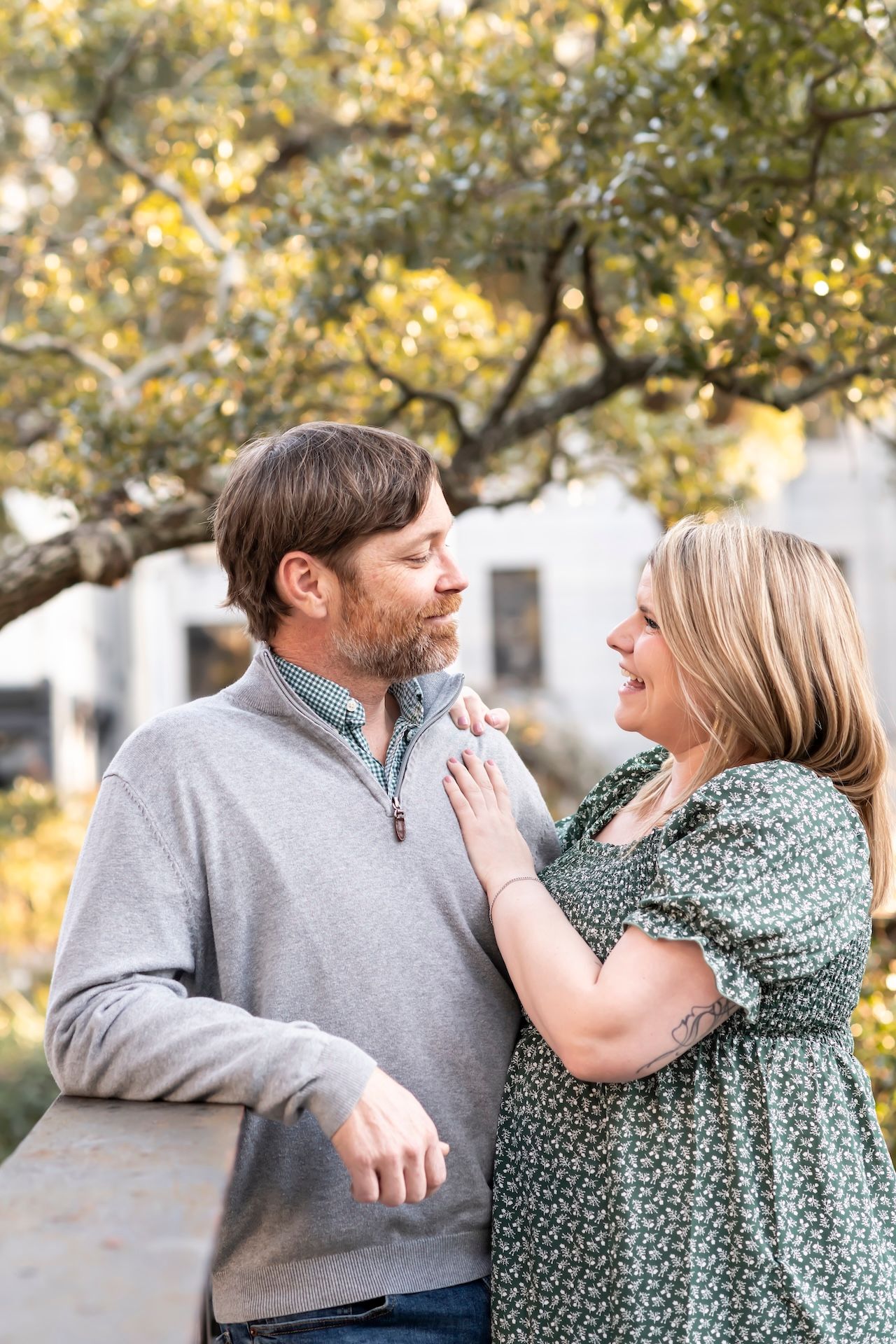 A couple in casual wear sharing a romantic moment on a bridge with fall foliage in the background.