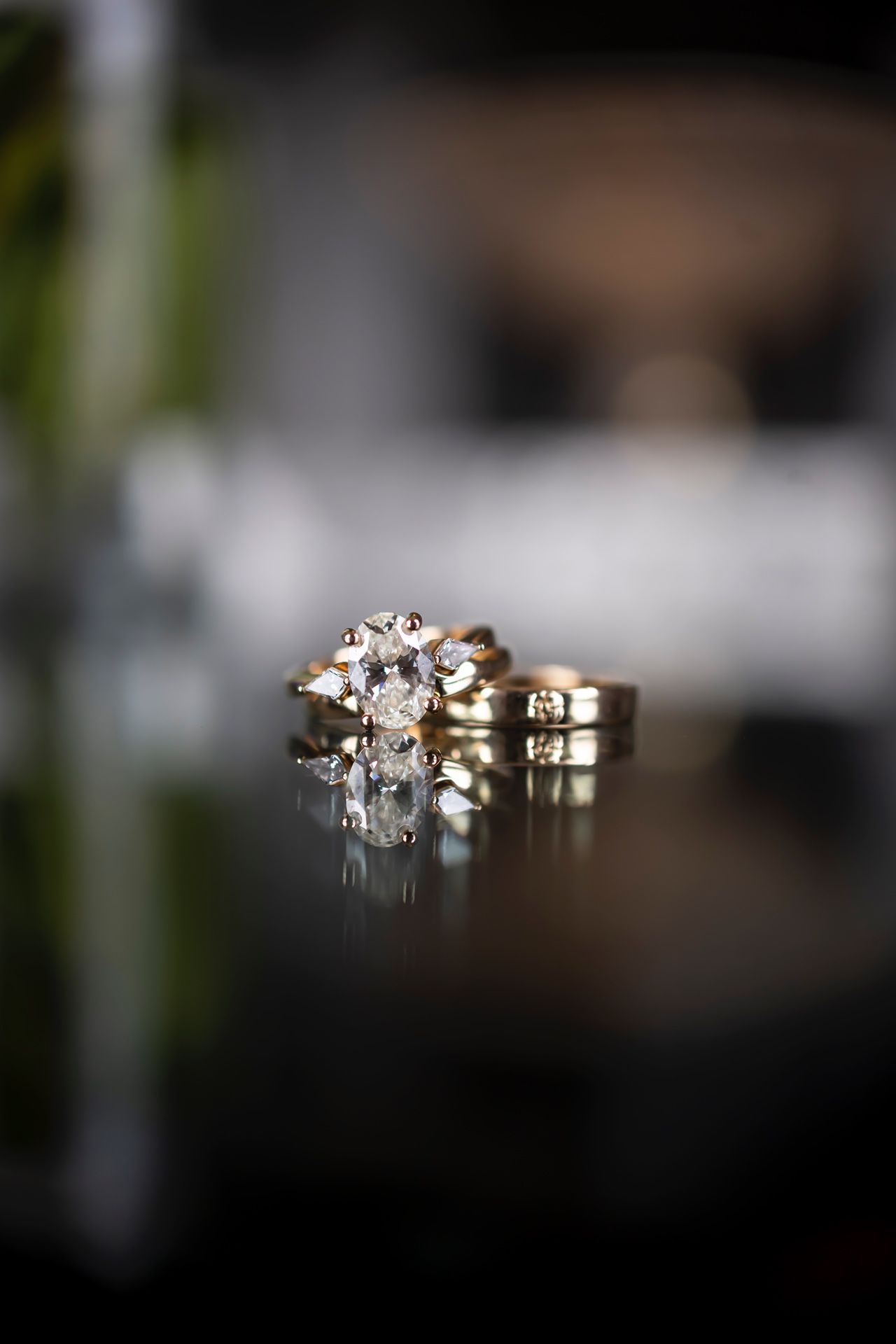 Wedding rings with a large diamond engagement ring reflecting on a dark glossy surface in an artistic macro shot.