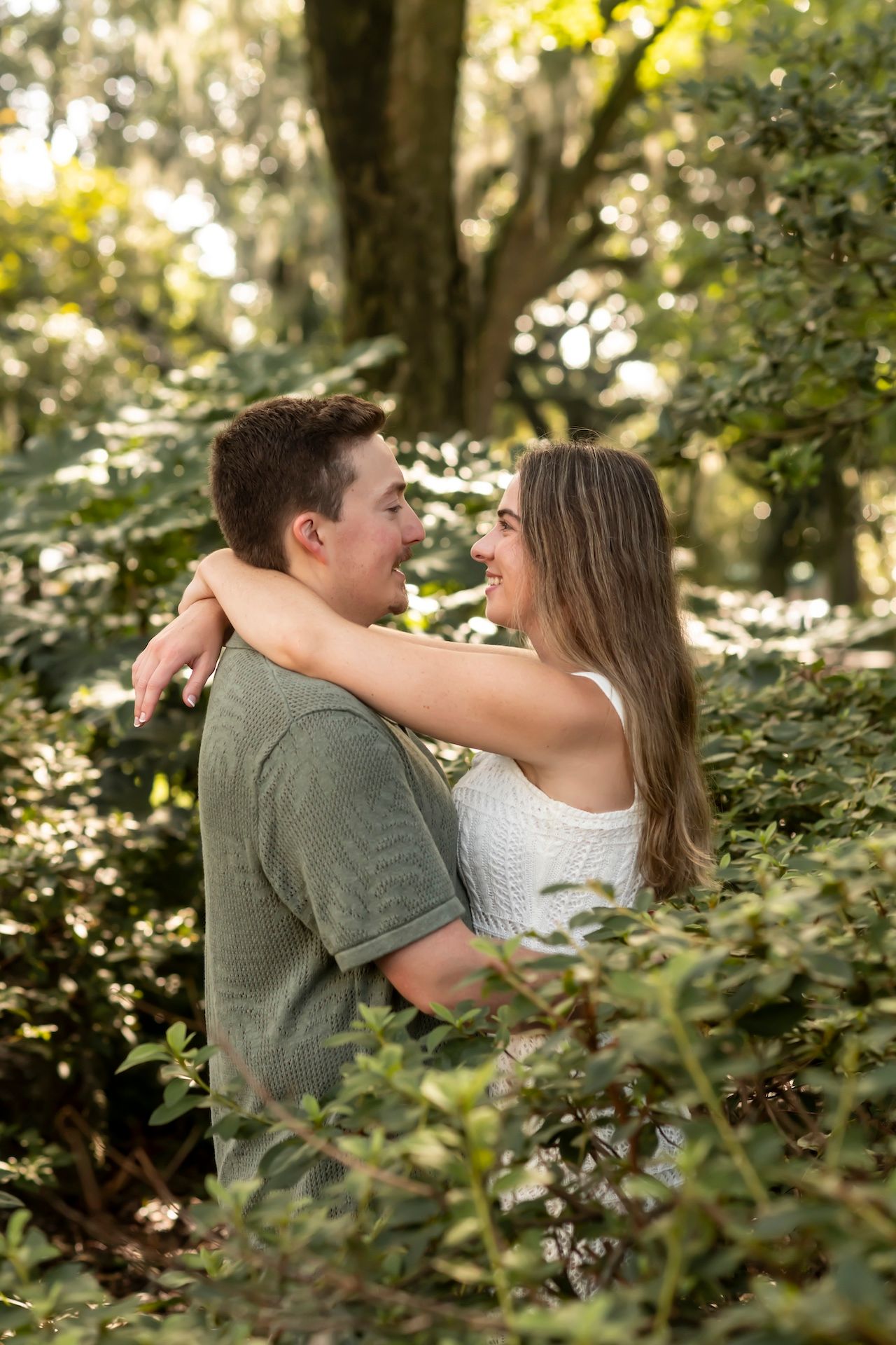 Romantic couple sharing an intimate moment outdoors among leafy green foliage in natural lighting.