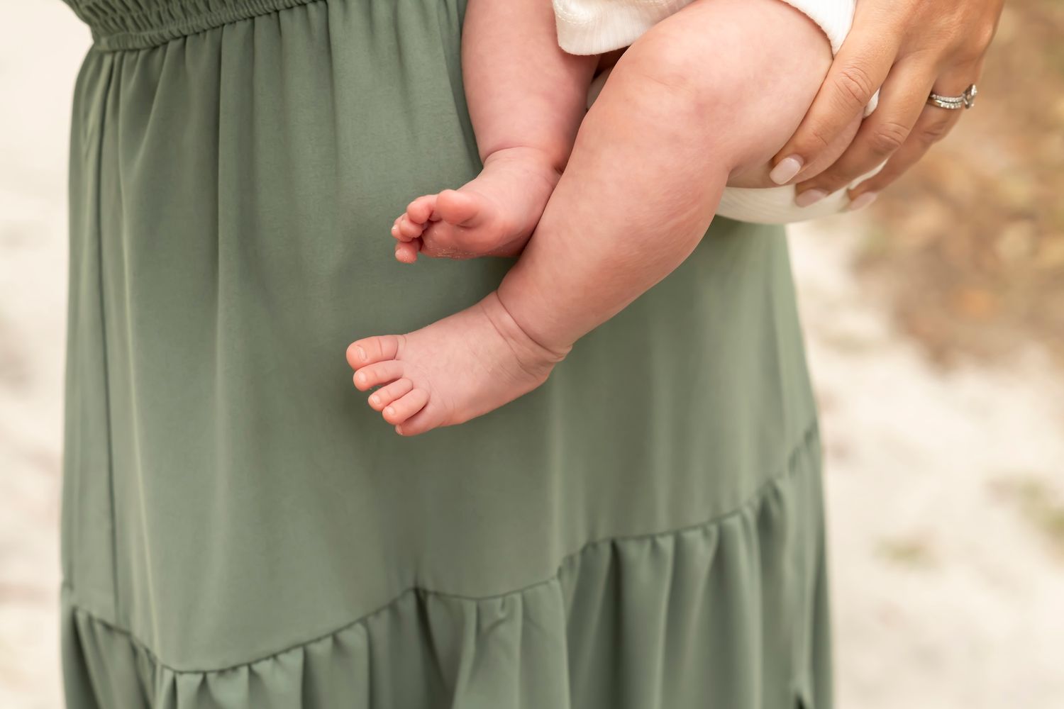 Young child's bare feet stand next to long olive green dress on light colored floor.