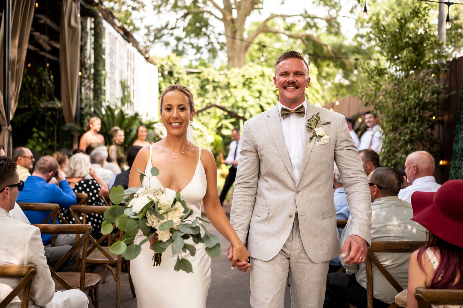 Newlywed couple walks down aisle at outdoor garden wedding ceremony with guests seated on either side at Cha Bella in Savannah.
