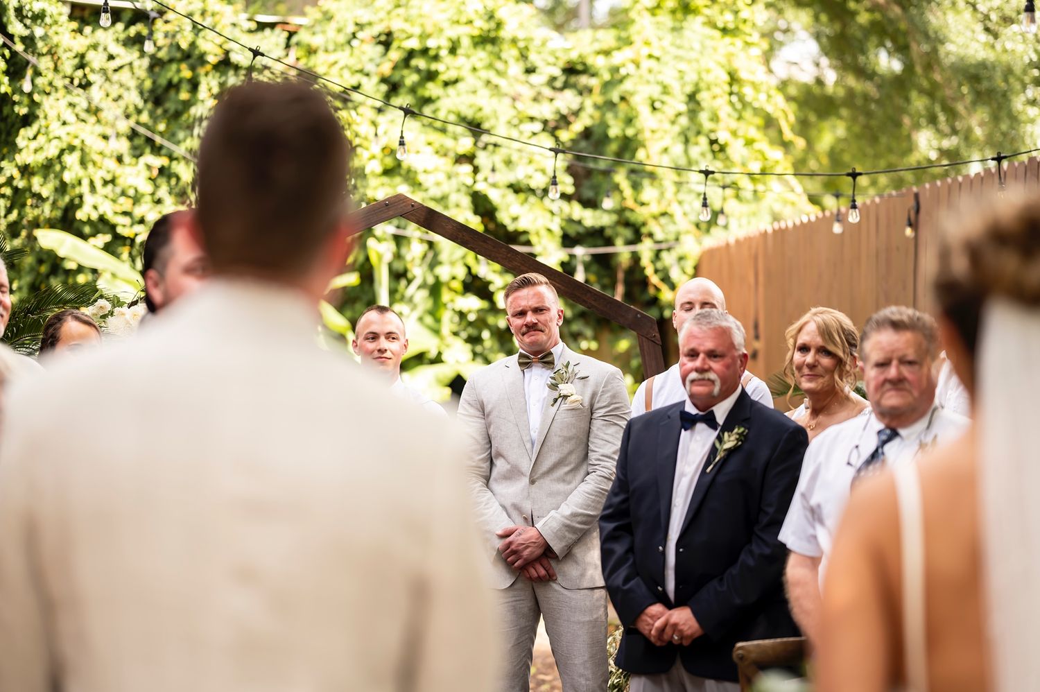 Wedding ceremony attendees smile in joyful anticipation during an outdoor garden celebration.