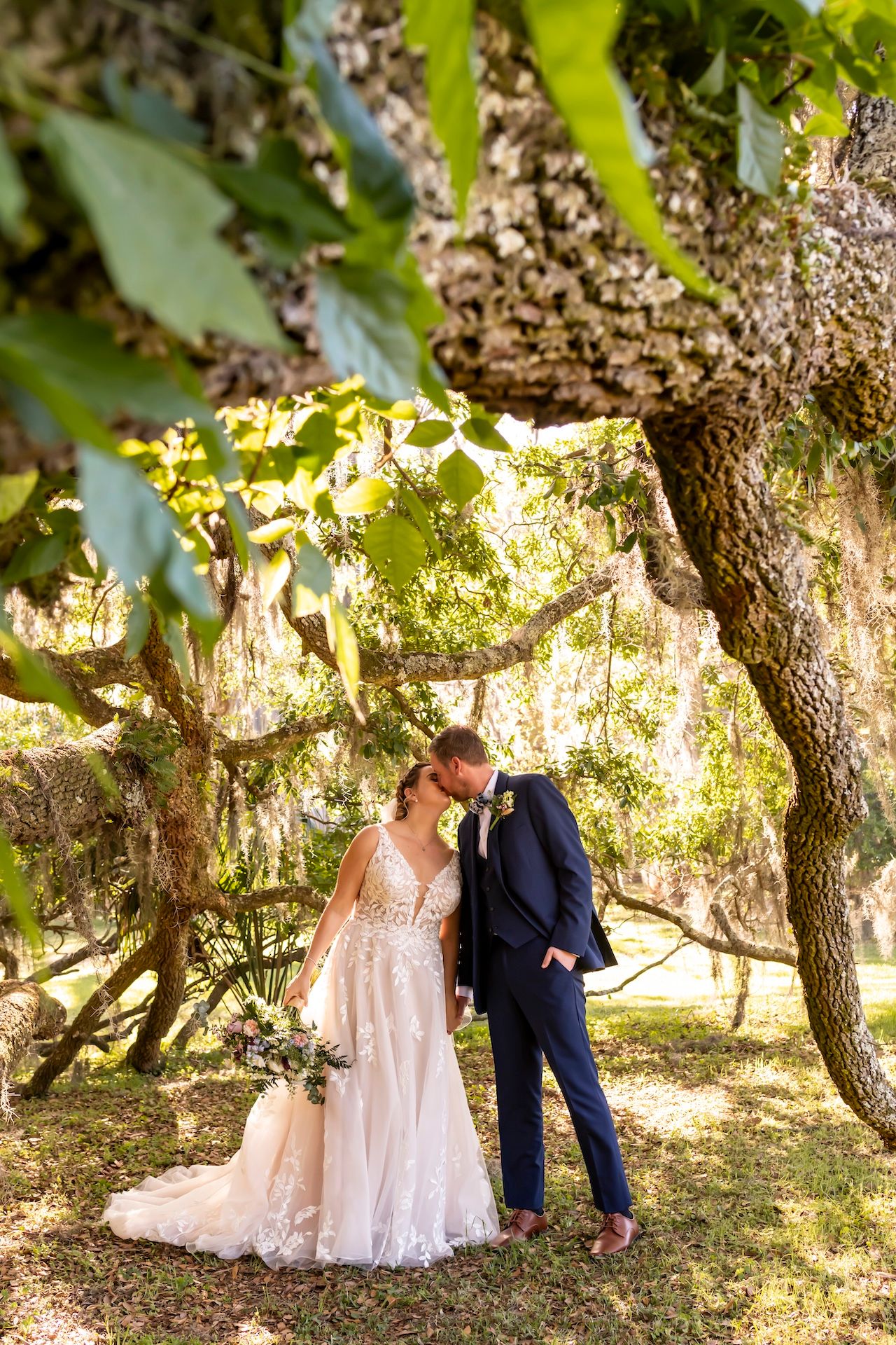 A couple shares an intimate moment under moss-draped trees in a romantic garden setting.