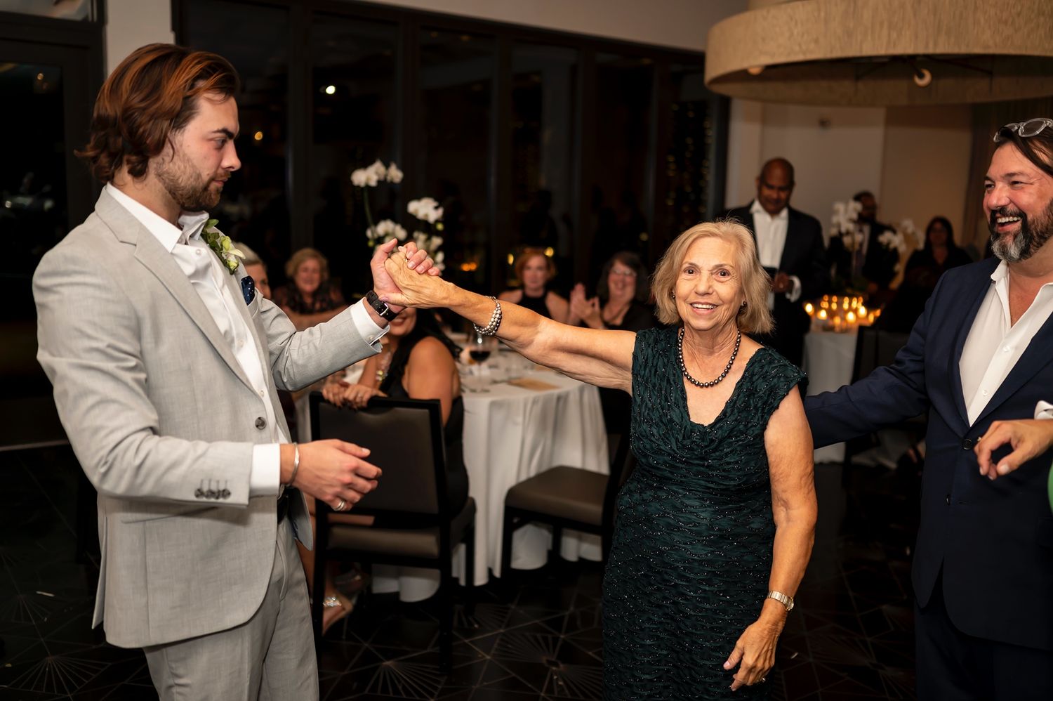 Wedding guests dance and celebrate on a dark dance floor at an evening reception party.