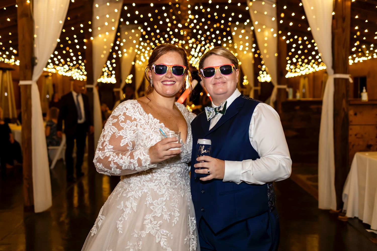 Happy couple celebrates at wedding reception under twinkling lights in rustic barn venue.