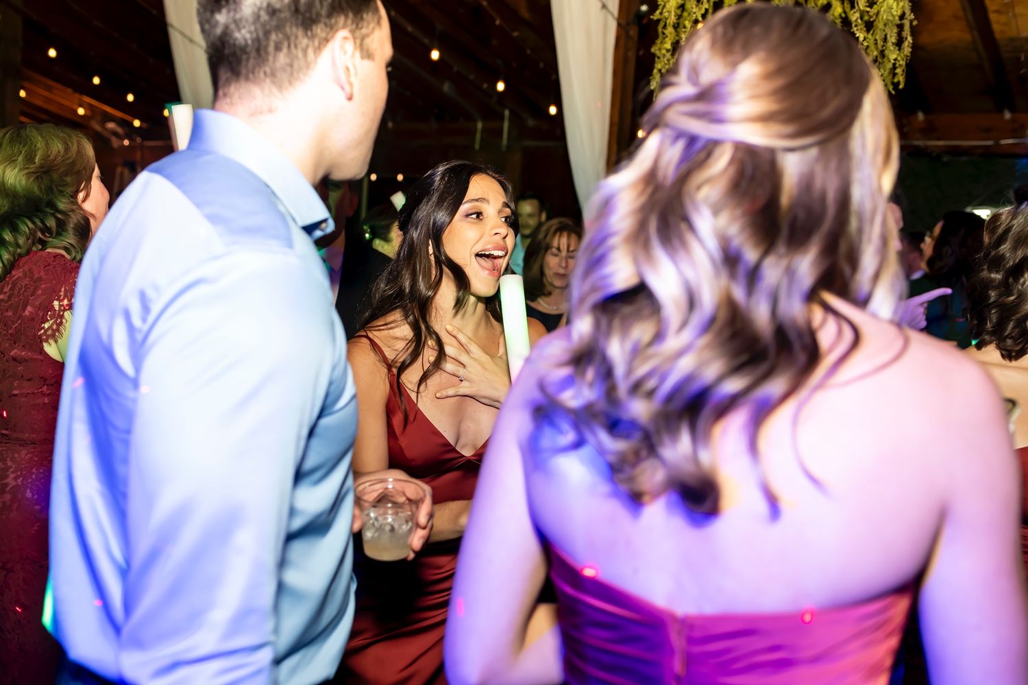 People chat and socialize at a dimly lit evening event with colorful lighting and a festive atmosphere.