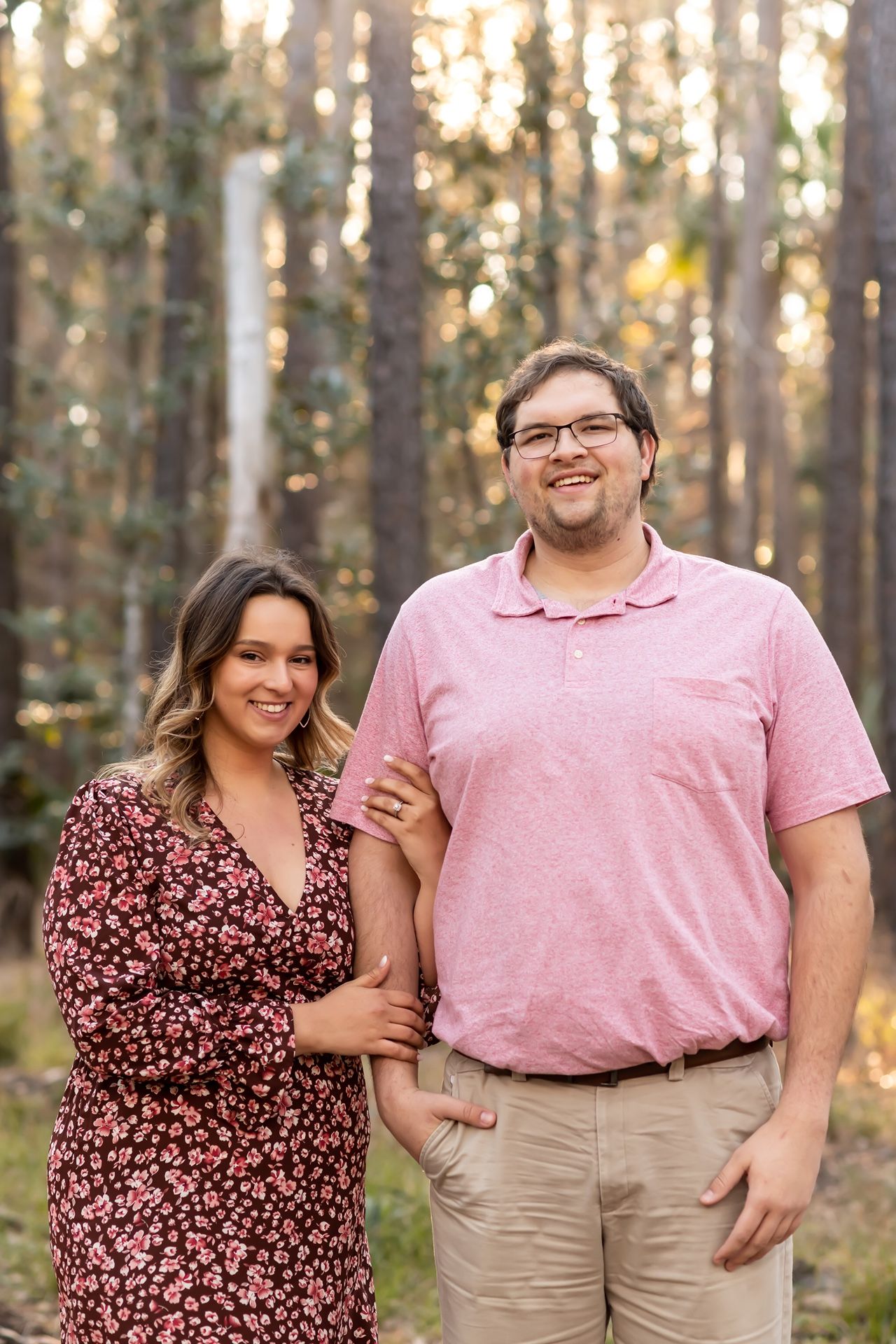 A couple poses together in a forest setting wearing coordinated pink and floral outfits.