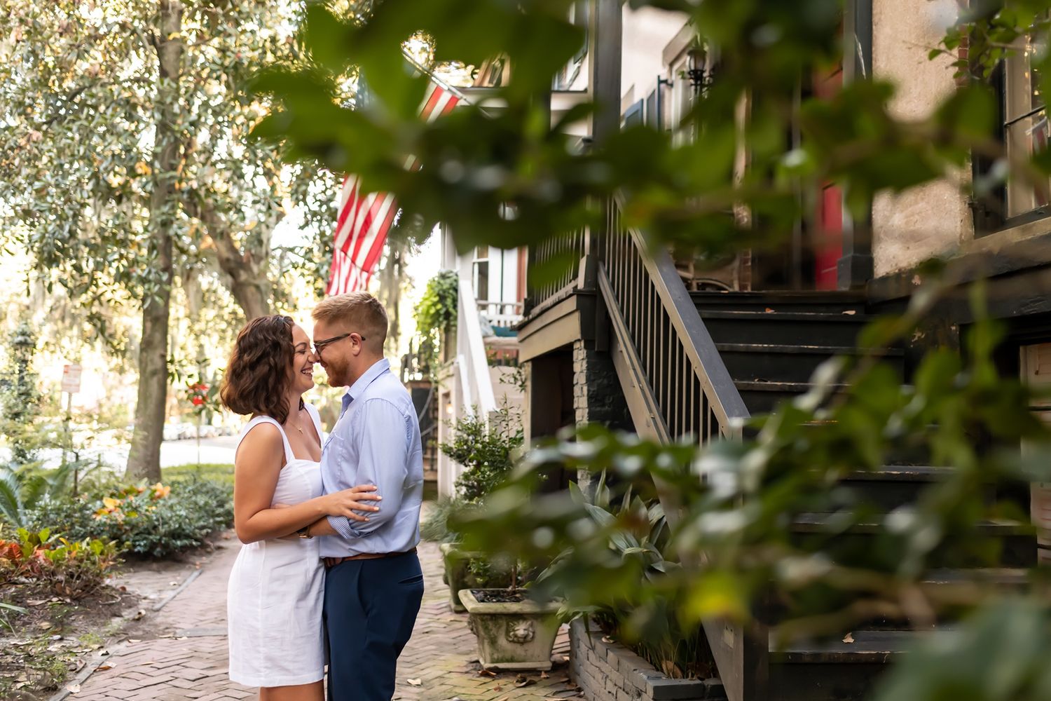 A couple embraces in a romantic moment outside a building with stairs and greenery in the foreground.