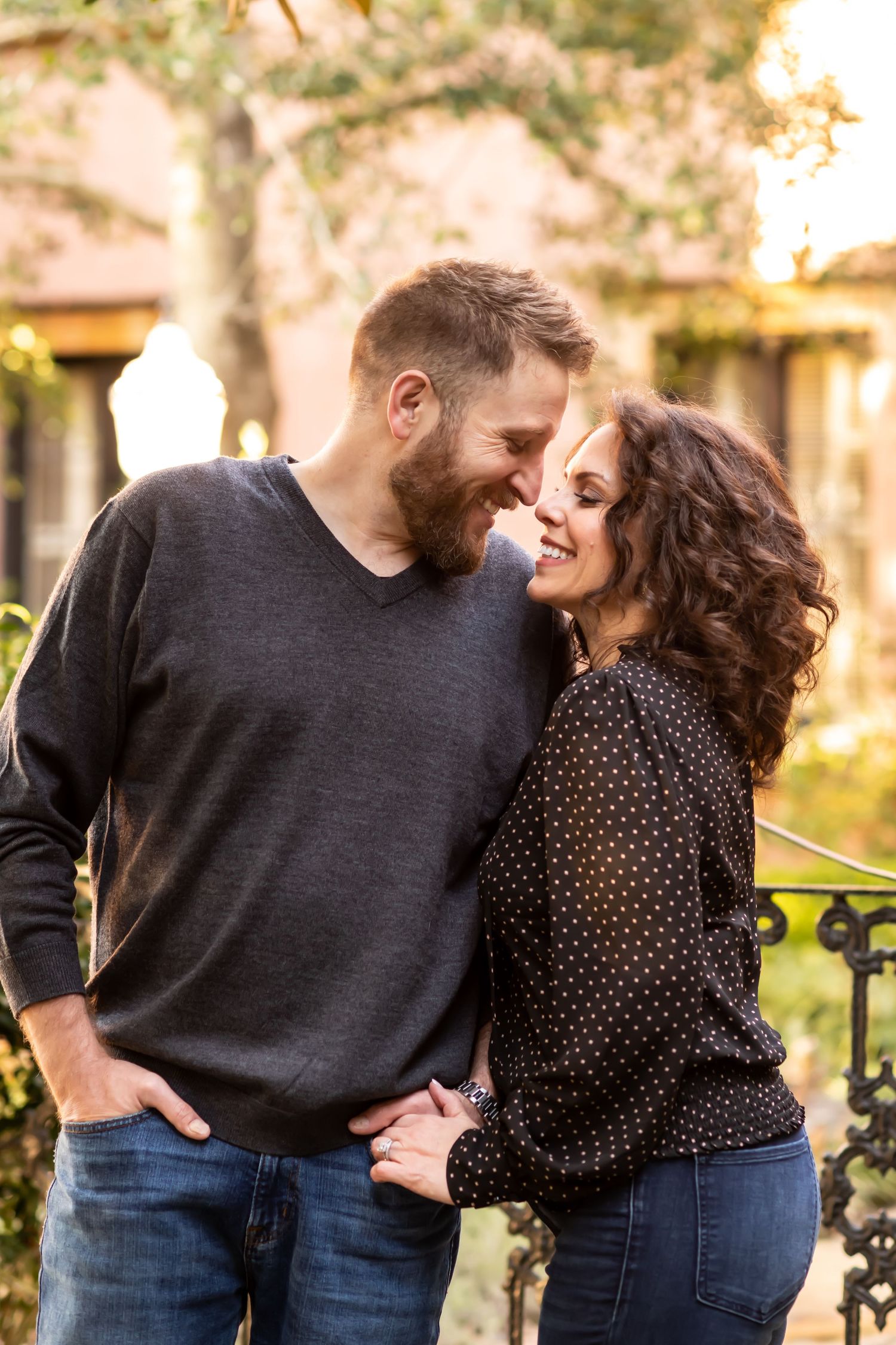 Couple sharing an intimate moment and laughing together outdoors by an iron railing during golden hour.