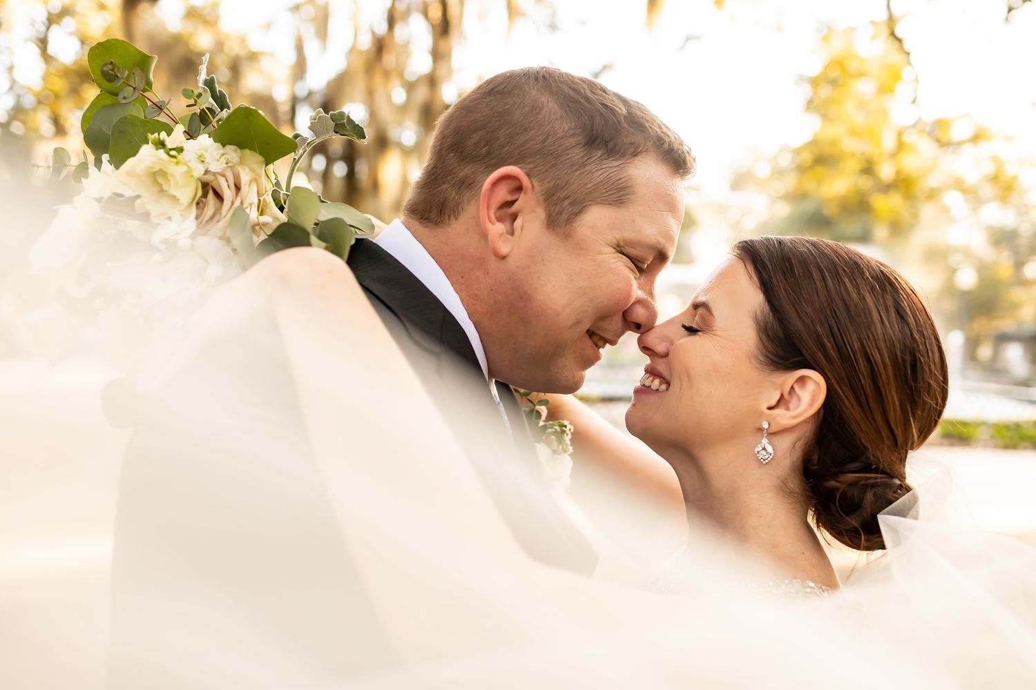 Close-up romantic portrait of newlyweds sharing a tender moment together at sunset outdoors.
