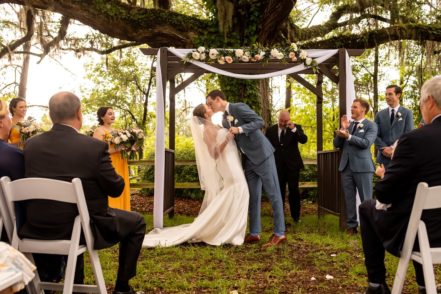 A series of outdoor wedding ceremony photos capturing guests gathering under white fabric draping between trees at sunset.