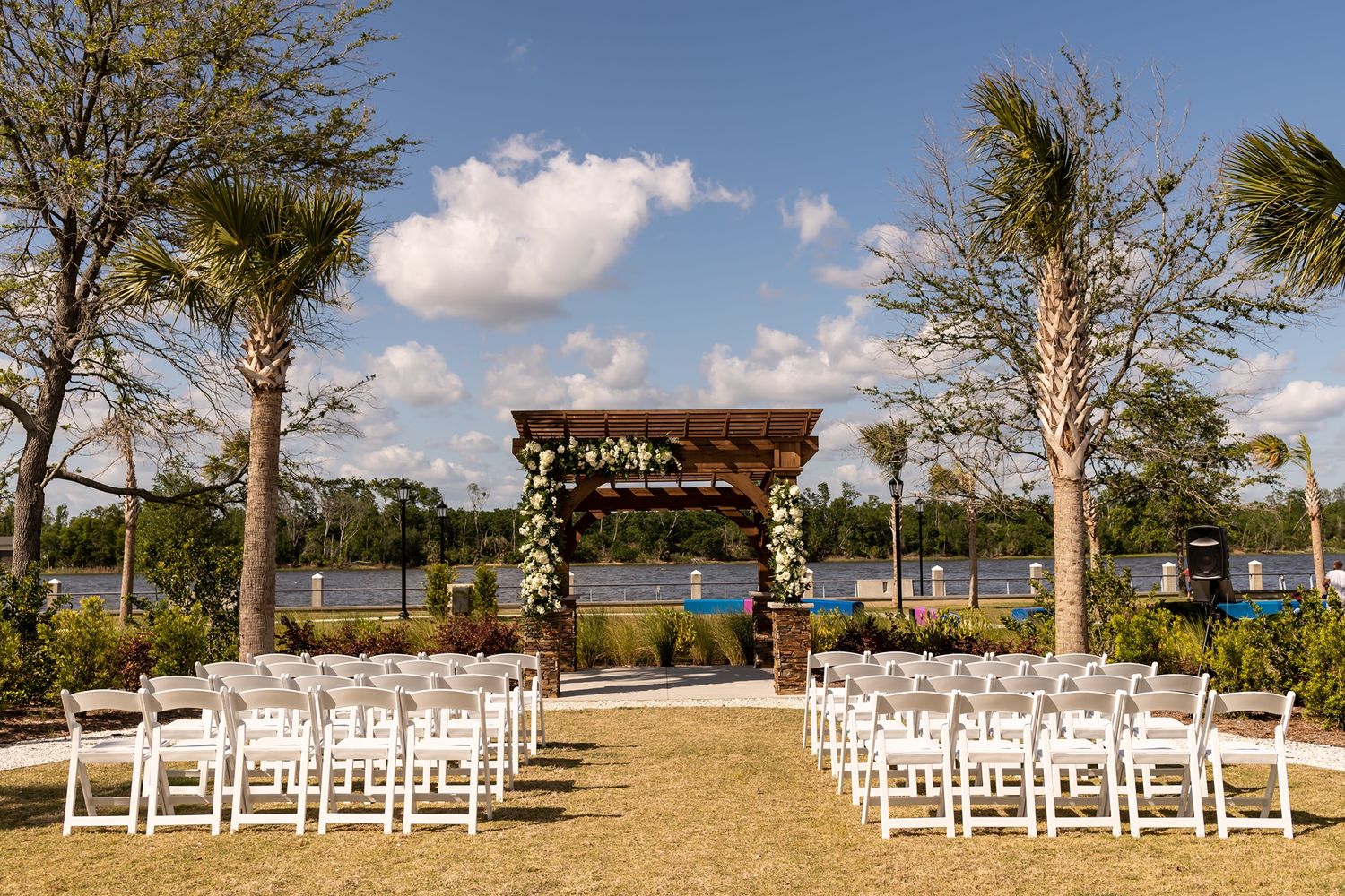 Panoramic view of an outdoor wedding ceremony setup with white chairs and a wooden arbor overlooking a scenic location.