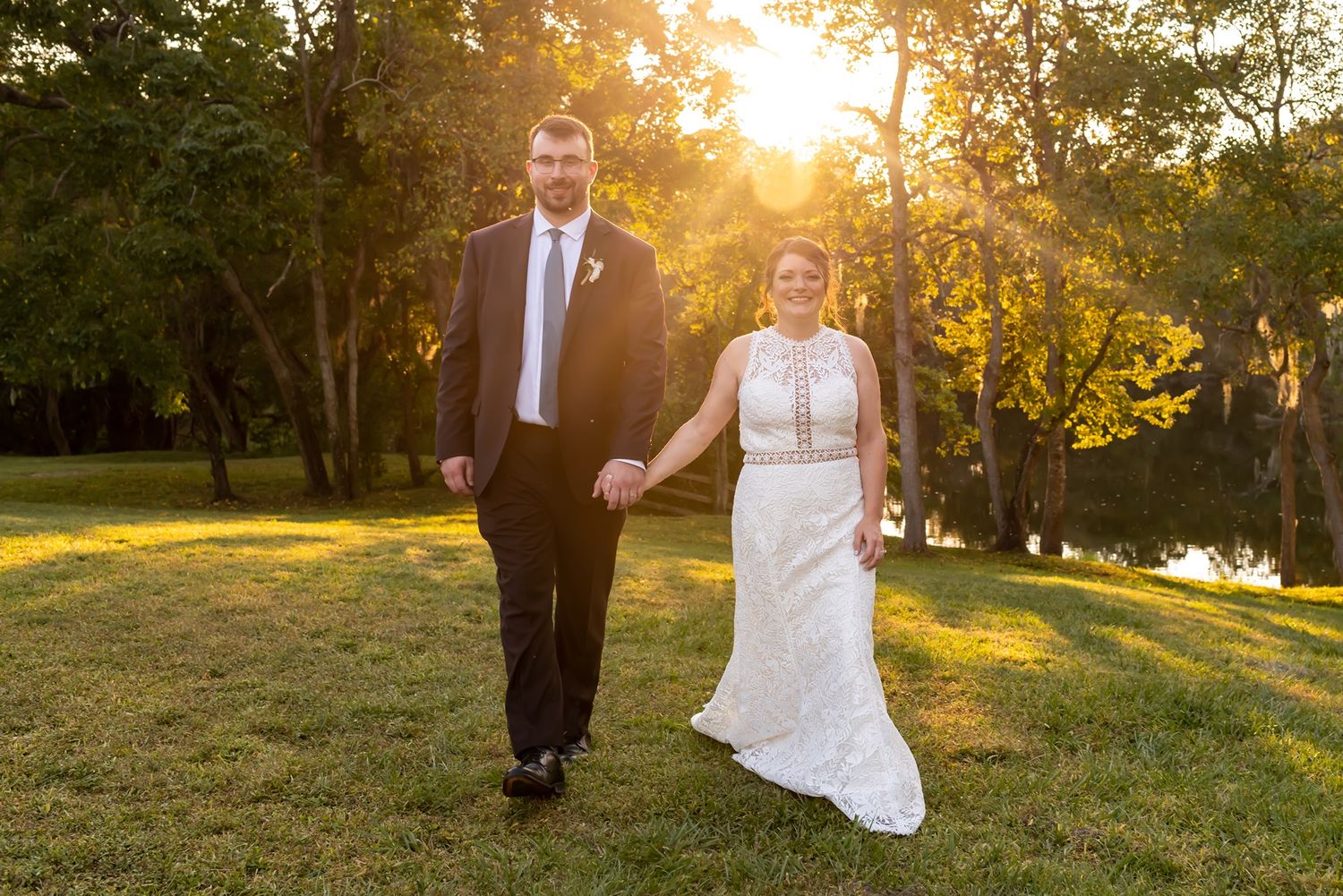 Wedding couple strolls together on grassy hill during golden sunset hour in romantic outdoor setting.