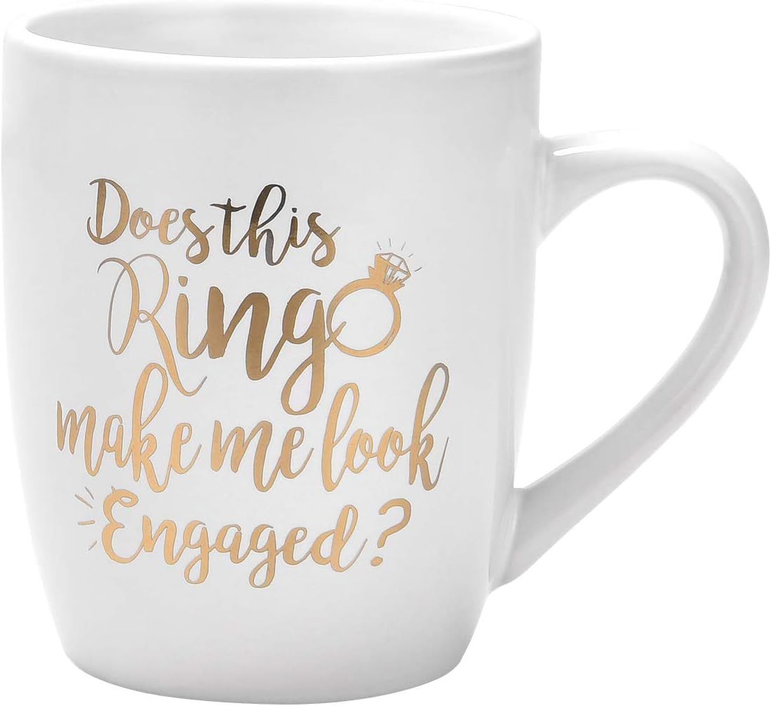 White ceramic coffee mug with gold text reading 'Does this ring make me look engaged?' and diamond ring design.