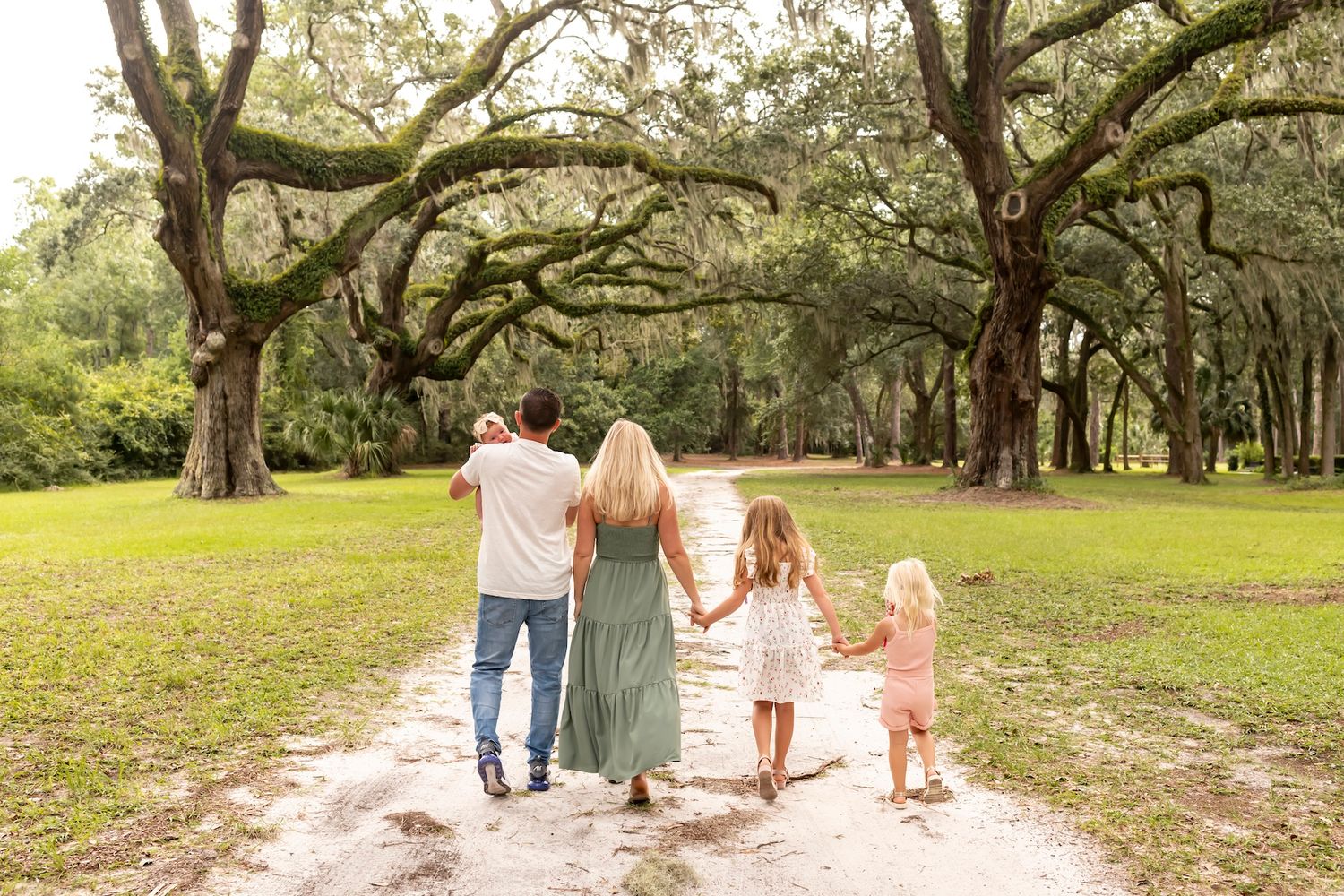Family enjoying a walk together down a tree-lined dirt path under majestic oak trees in a scenic southern landscape.