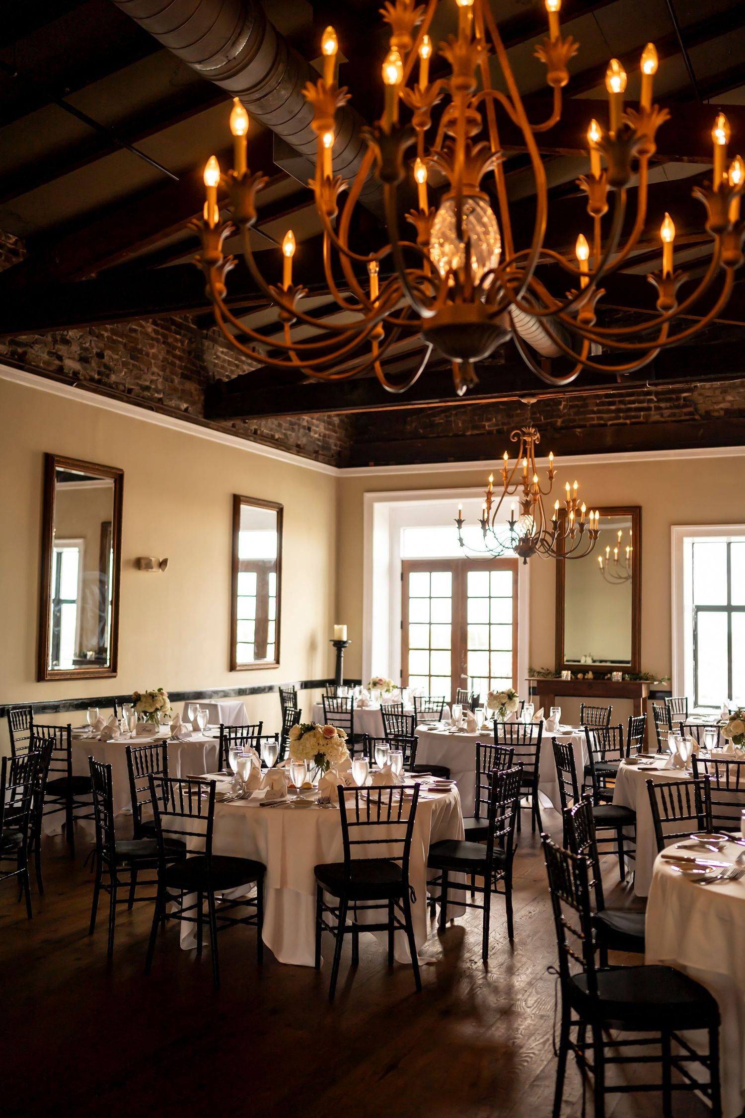 Elegant wedding reception venue with crystal chandeliers, exposed brick walls and round tables set with cream linens.
