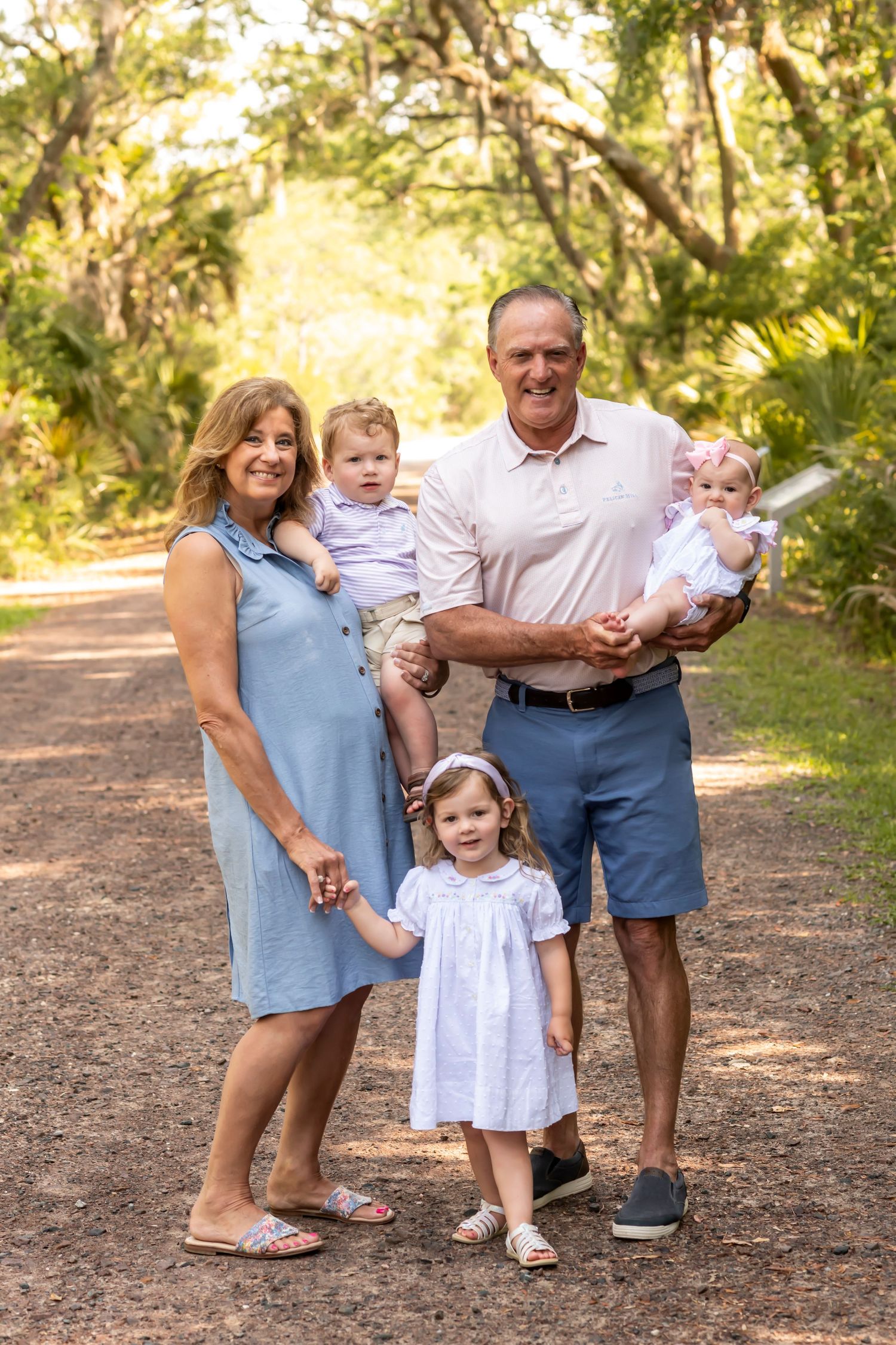 Family group poses together on a tree-lined nature path in golden sunlight.