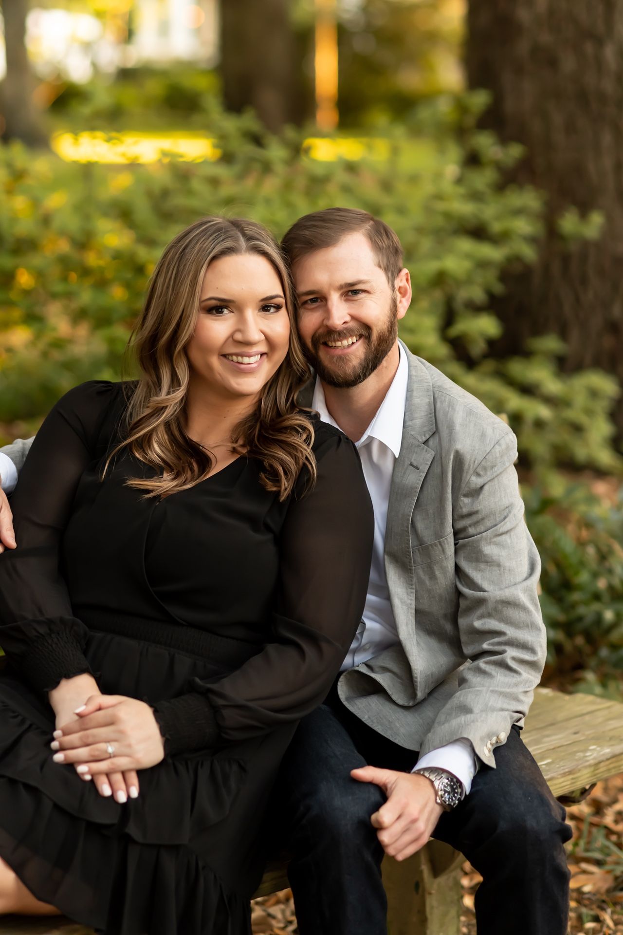 A couple in formal attire poses together outdoors for romantic autumn engagement photos in a park setting.