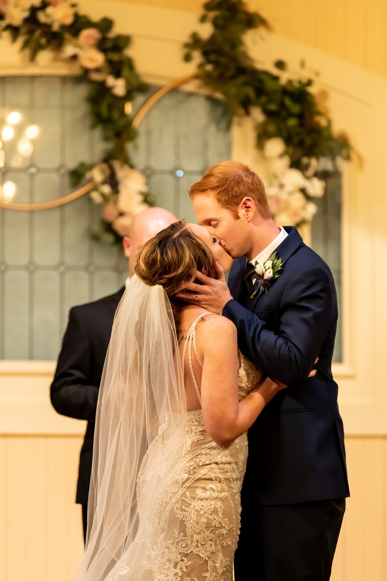 Romantic moment at a wedding ceremony with floral arch decorations and candlelight in the background.