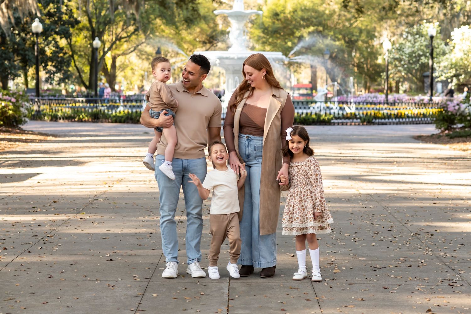 A family holds hands while taking a stroll together down a tree-lined pathway in a scenic park setting.