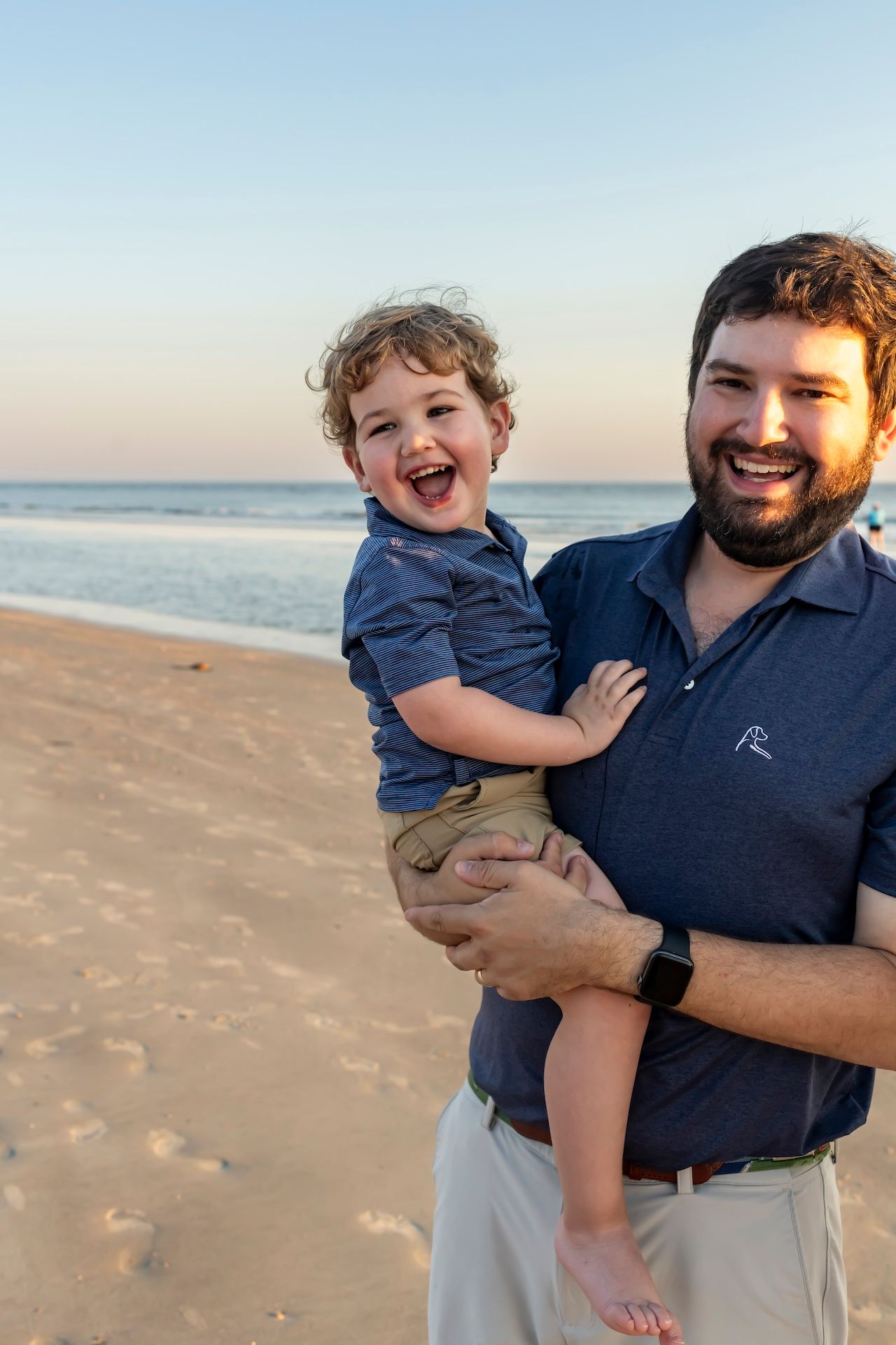 Joyful parent and child sharing a laugh together on a sandy beach at sunset.
