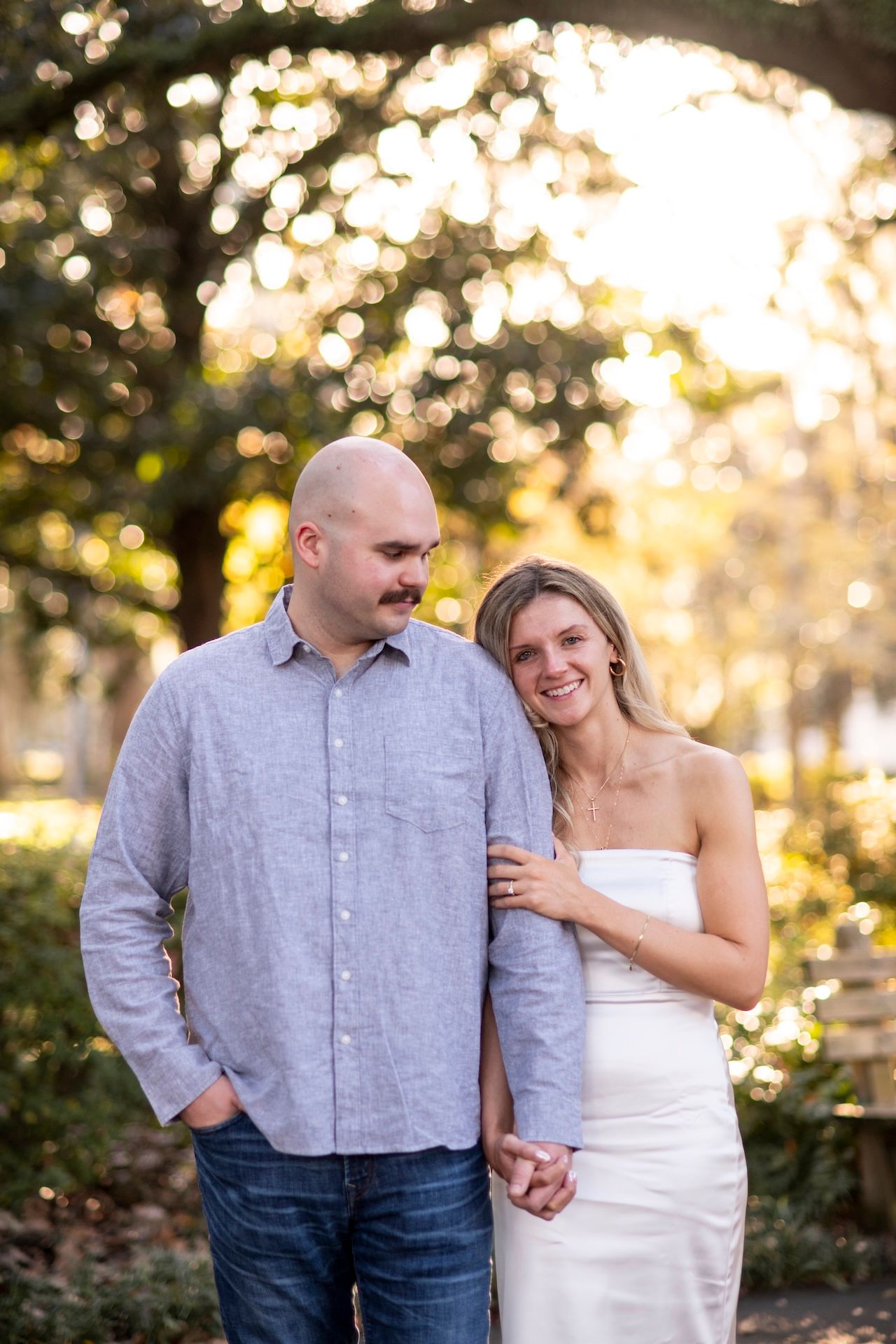 A couple shares a tender moment outdoors at sunset with beautiful golden bokeh lighting in the background.