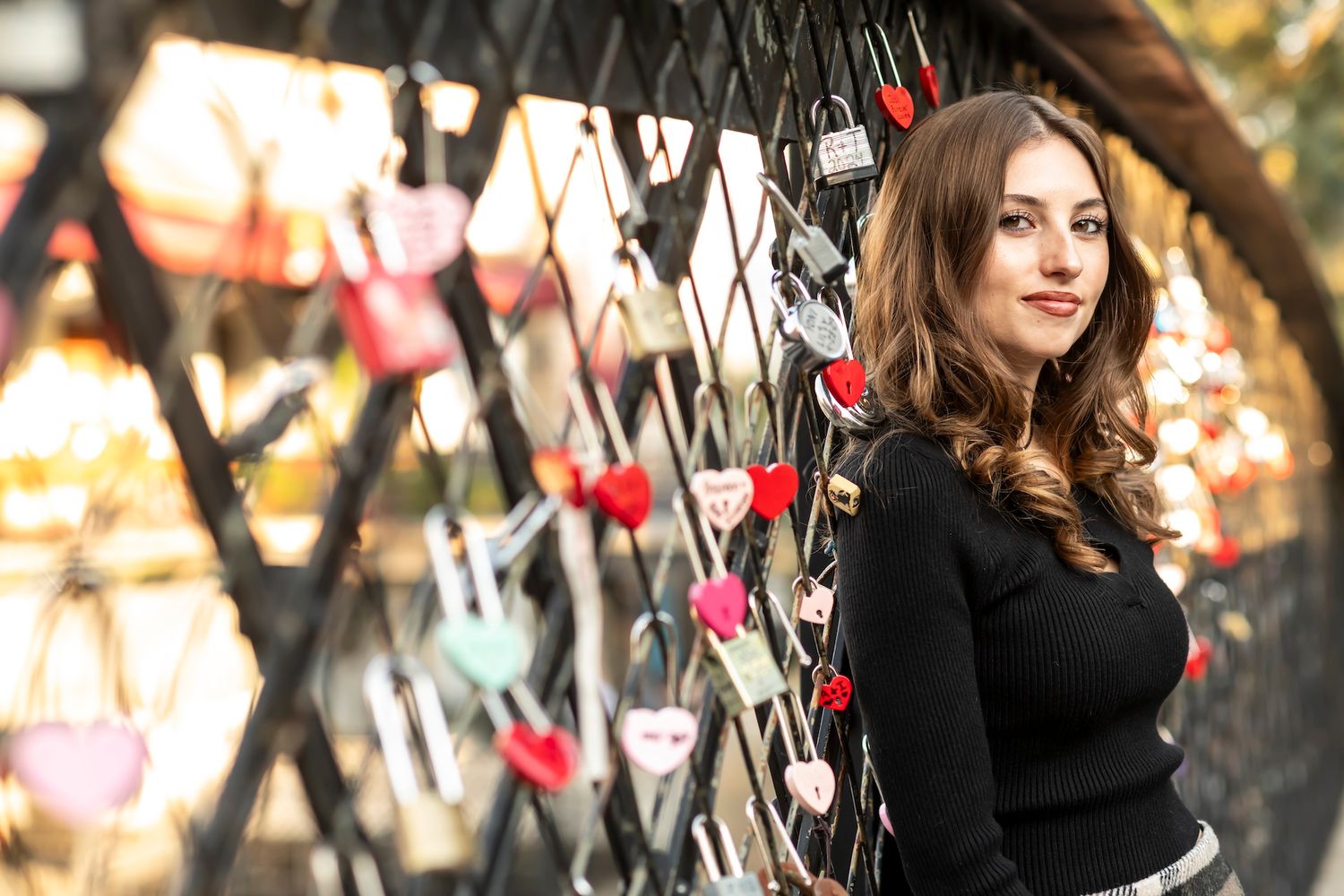 Woman in black sweater poses against graffiti wall with colorful lights in background.