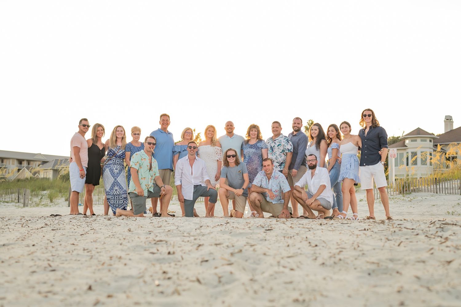 A large group in coordinated blue and white outfits poses together on a sandy beach at sunset.