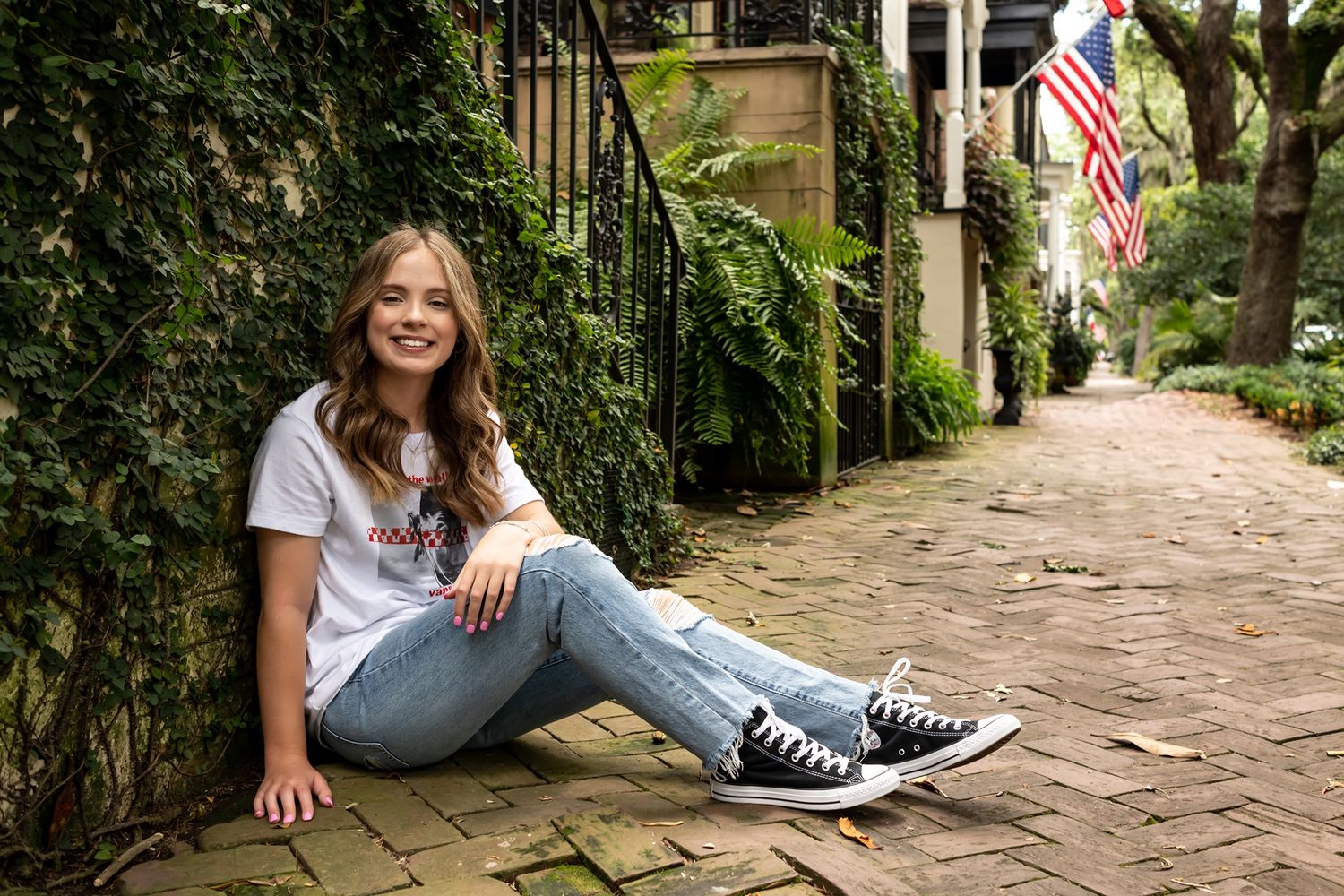 Someone sits on a brick sidewalk with ivy-covered walls and an American flag visible in the Charleston historic district.