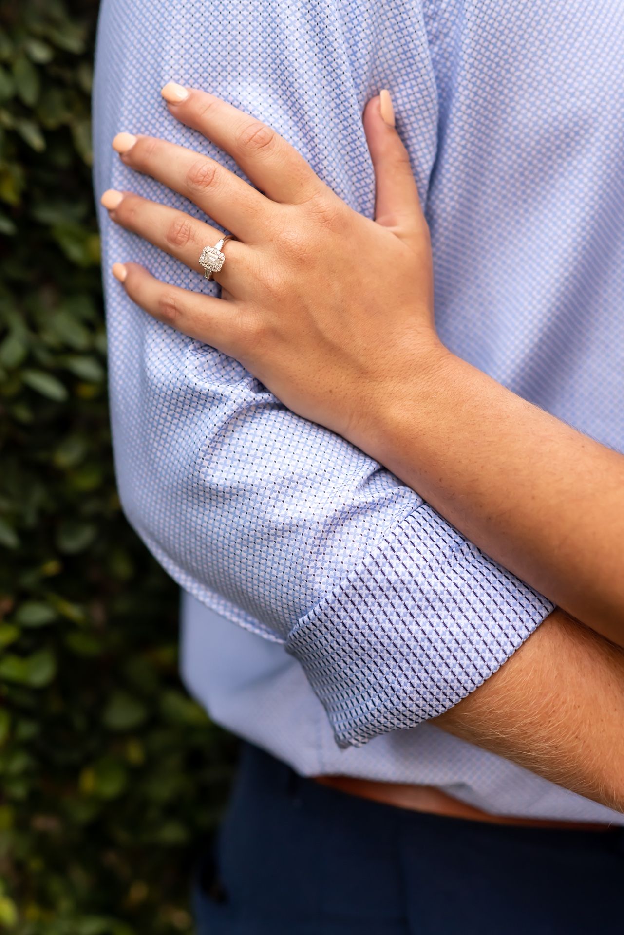 Close-up of a hand wearing an engagement ring resting on a person wearing a light blue dress shirt.