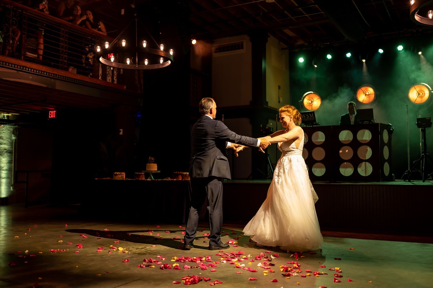 A couple dances their first dance on a stage decorated with rose petals and illuminated by warm lighting and lanterns.