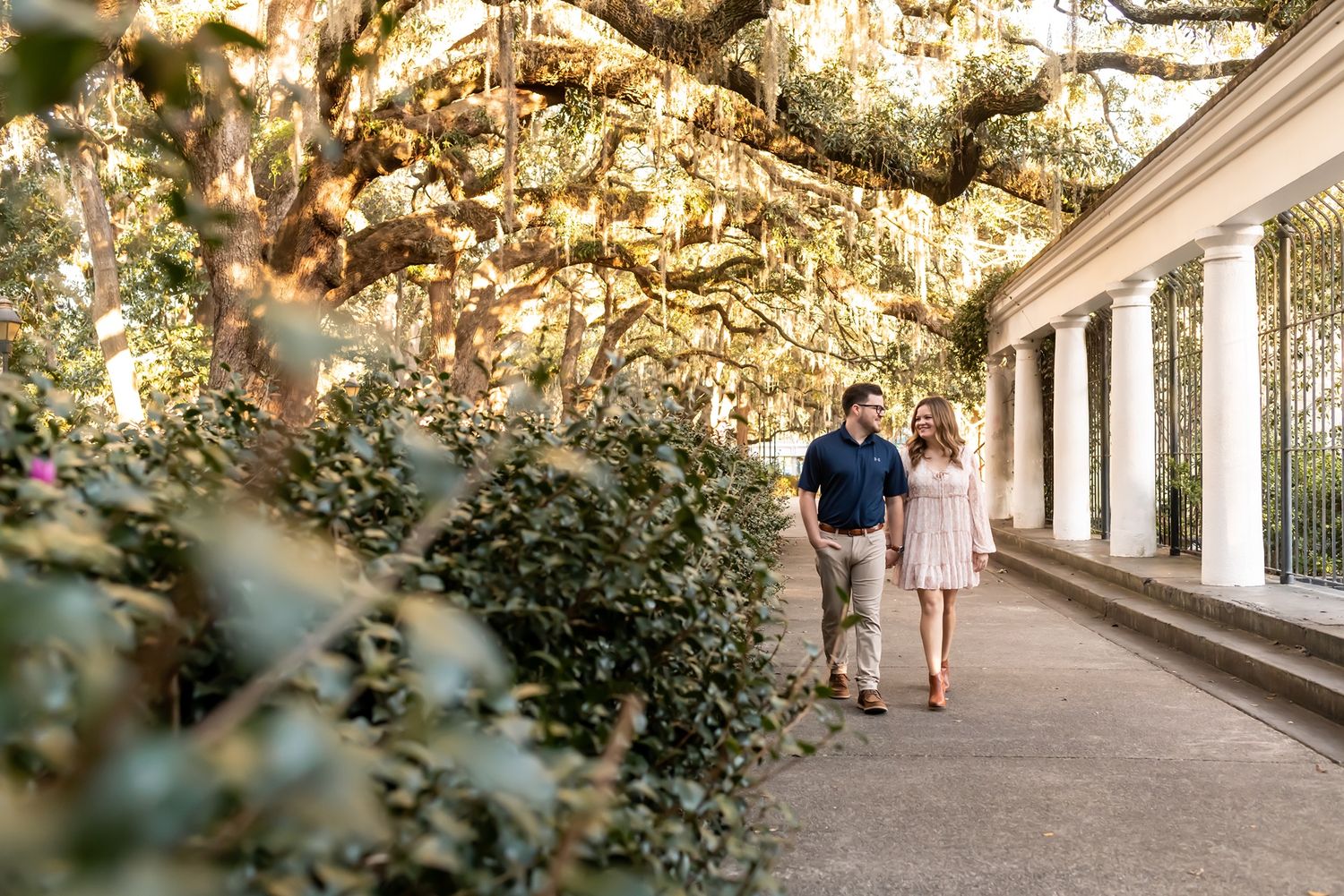 Couple walking together through a scenic covered walkway with lush greenery and natural lighting overhead.