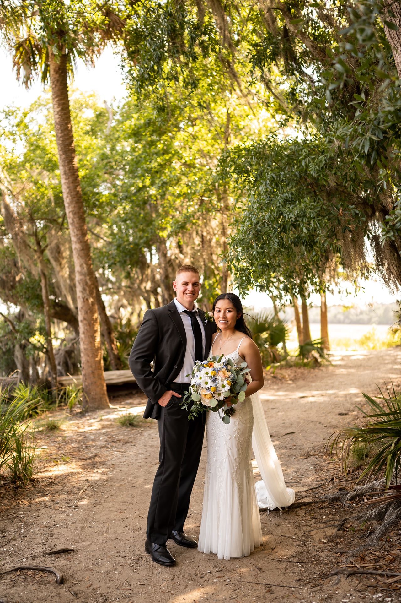 A wedding couple shares romantic moments in a sunlit wooded outdoor setting with natural golden lighting.