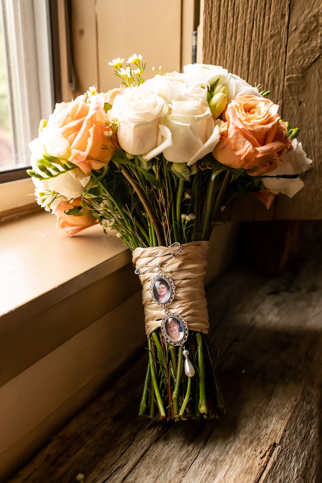 An elegant bouquet of peach and white roses wrapped in twine sits on a rustic wooden surface near a window.