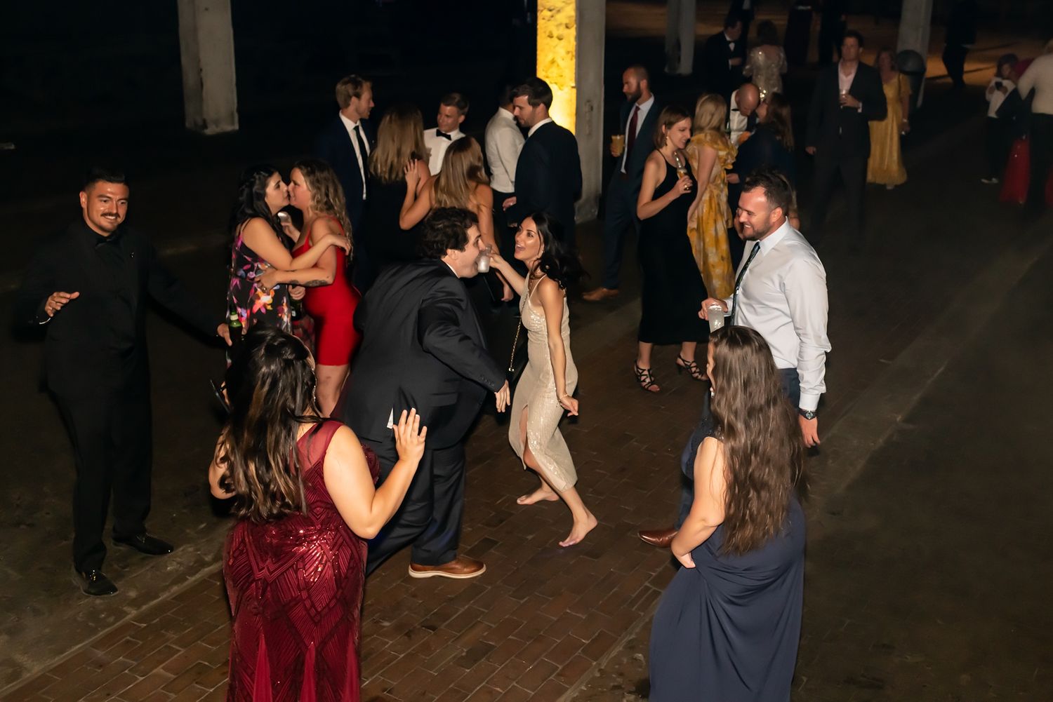 People dancing and socializing at a dimly lit formal event venue with multiple dancing couples visible on the floor.