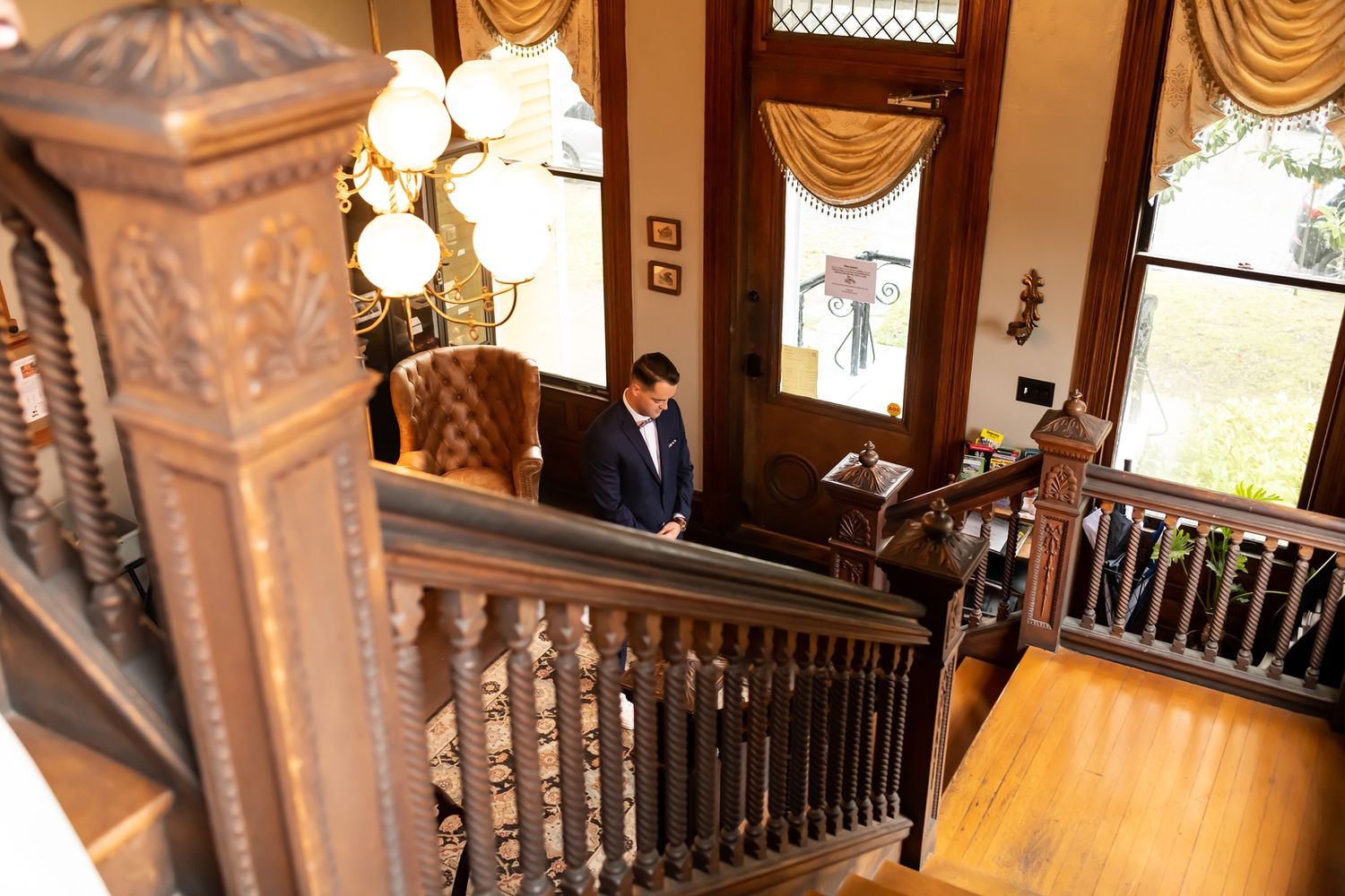 Interior view of an elegant Victorian staircase with ornate wooden railings and chandelier lighting in a historic mansion.