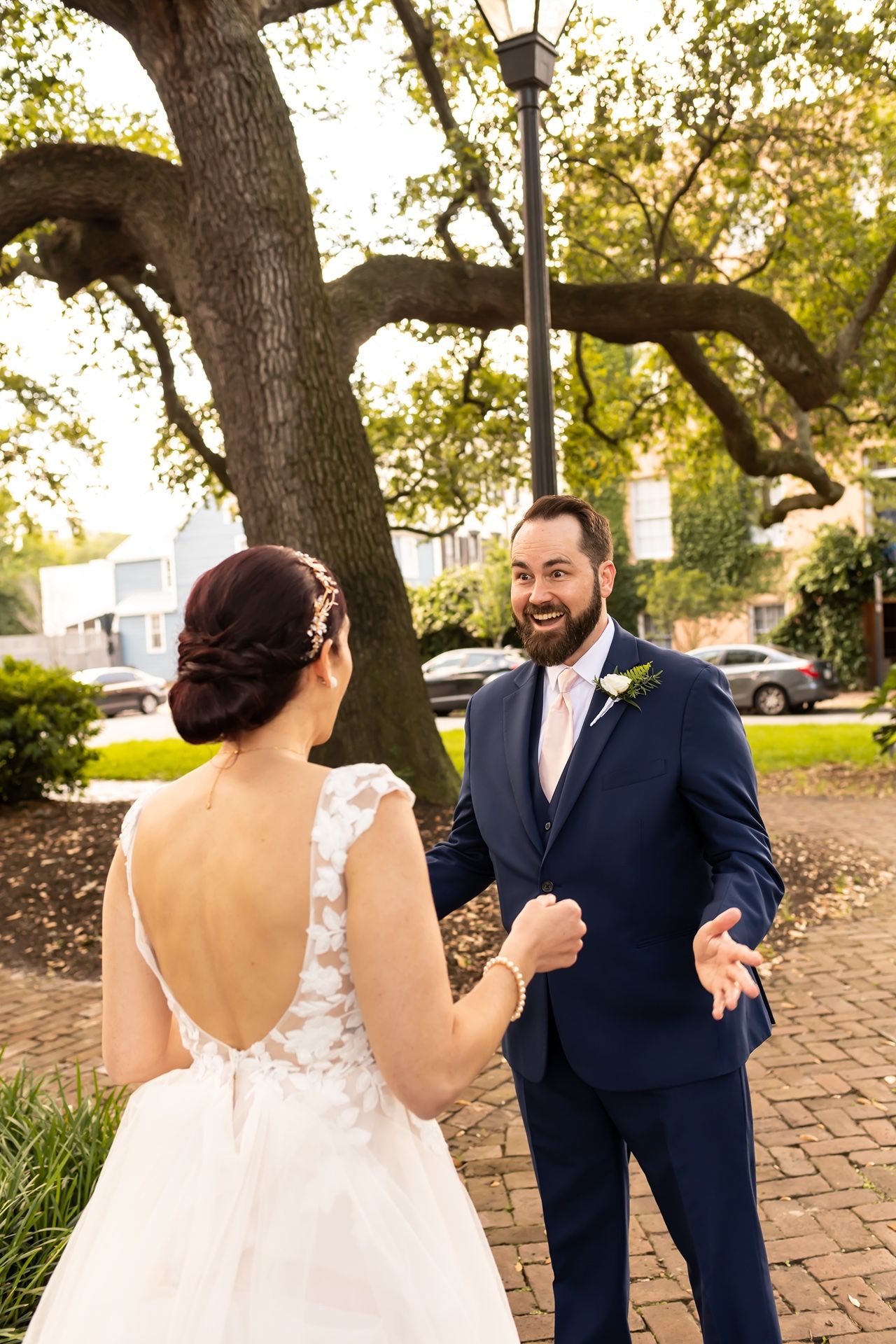 A bride and groom share their first look moment in a garden setting with golden sunlight filtering through trees.