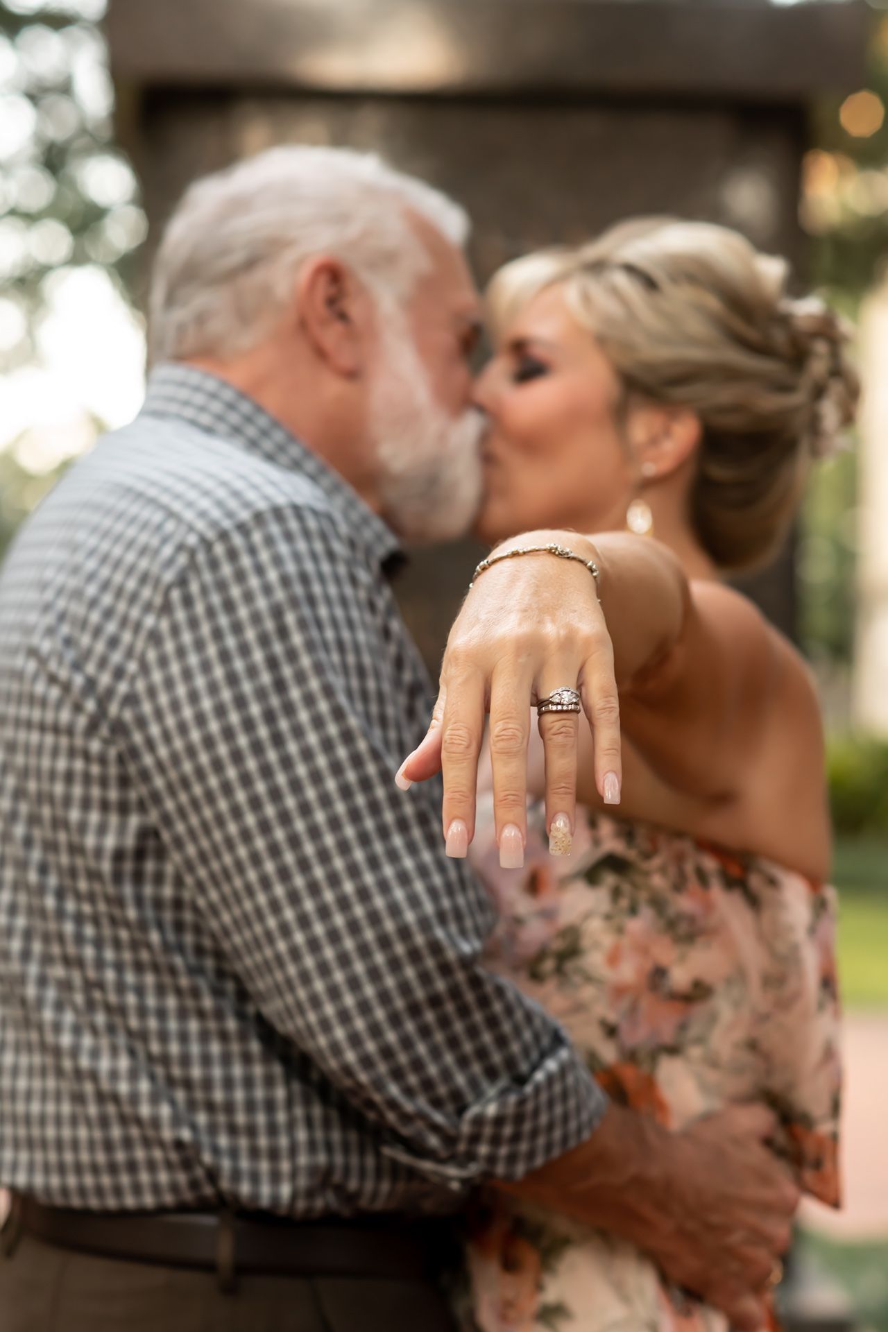 Close-up of an engagement ring on display as a couple embraces in a romantic outdoor setting during golden hour.