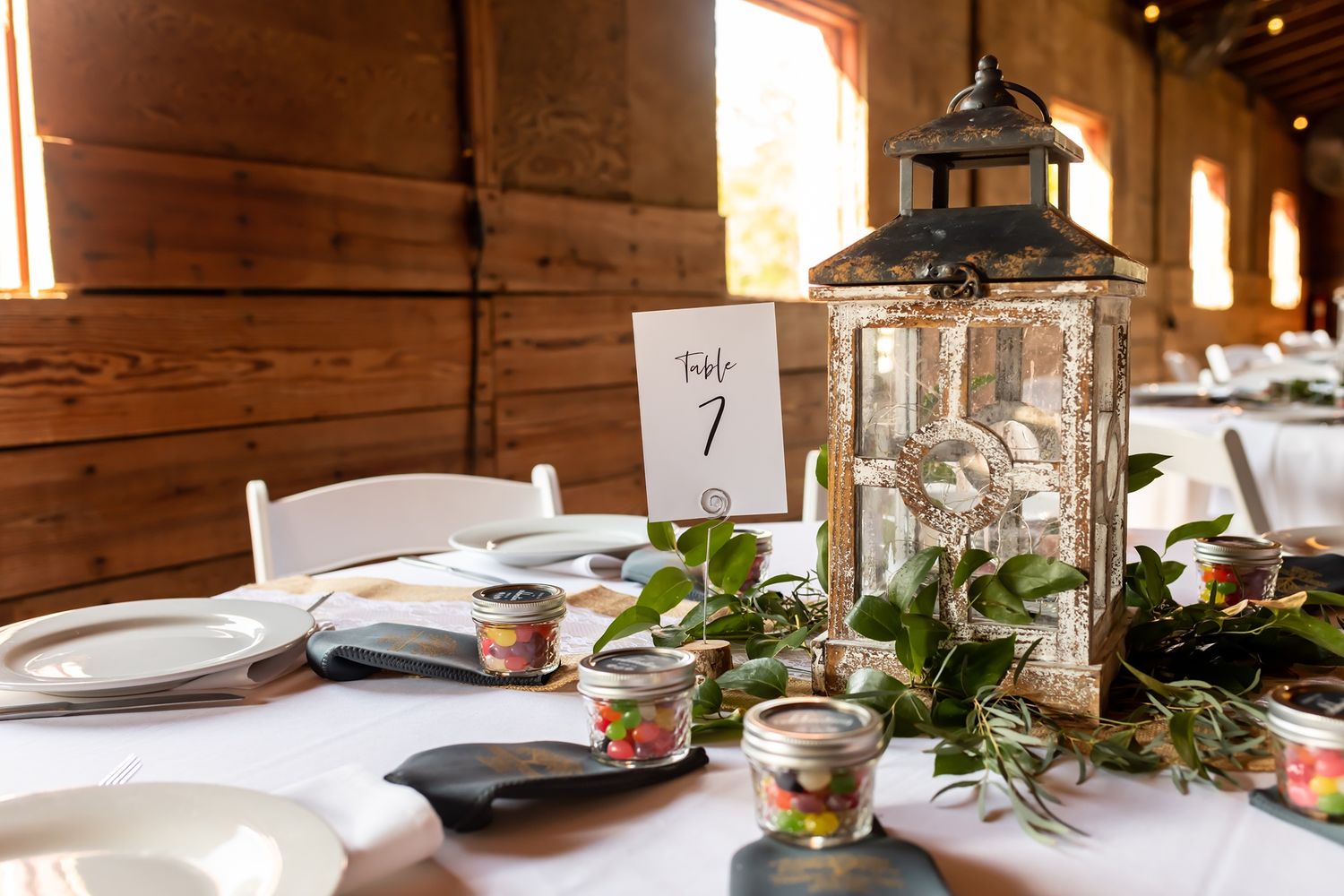 Wedding reception table setting with rustic lantern centerpiece, eucalyptus greenery, and table number one marker.