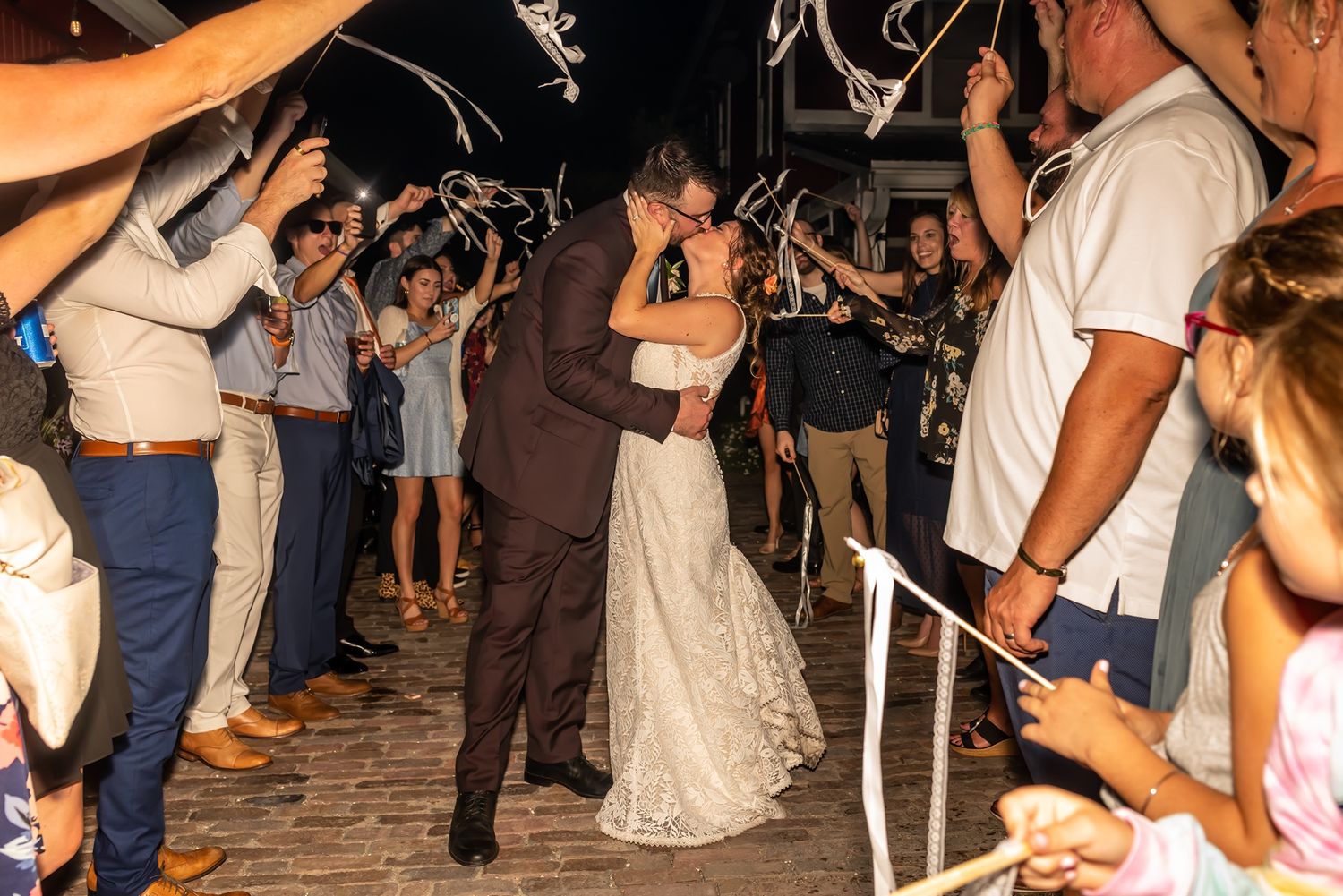 Newlyweds share an intimate dance surrounded by wedding guests holding sparklers on a brick patio at night.