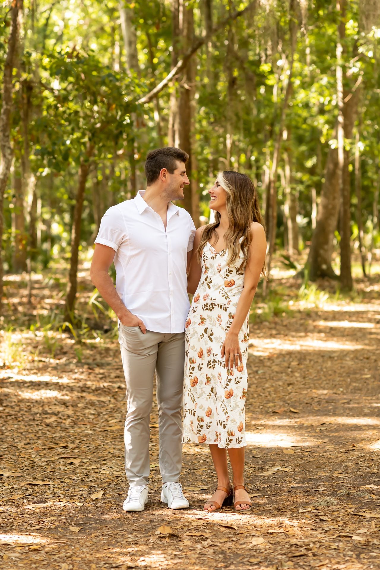 A couple shares intimate moments in a sun-dappled forest path during a romantic outdoor photoshoot.