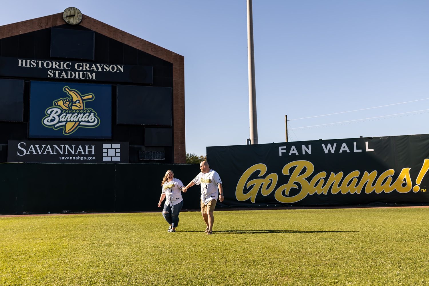 Historic Savannah Bananas baseball stadium with a black scoreboard and green grassy field on a sunny day.