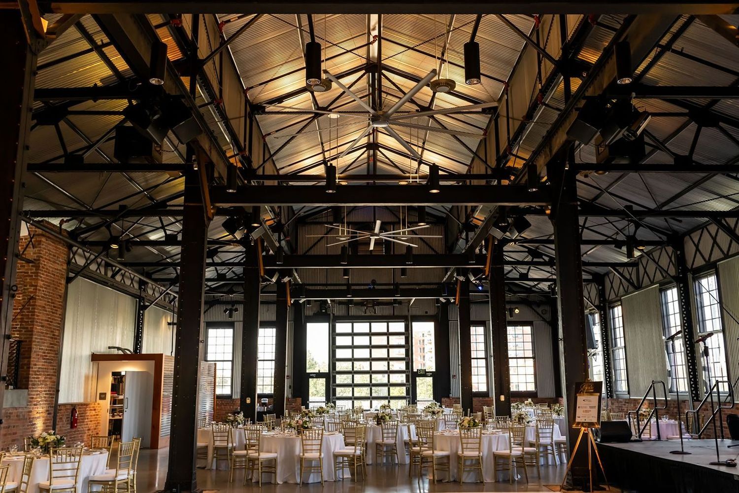 Industrial event venue with exposed beams and vaulted ceiling showcases modern reception tables set for a wedding celebration.