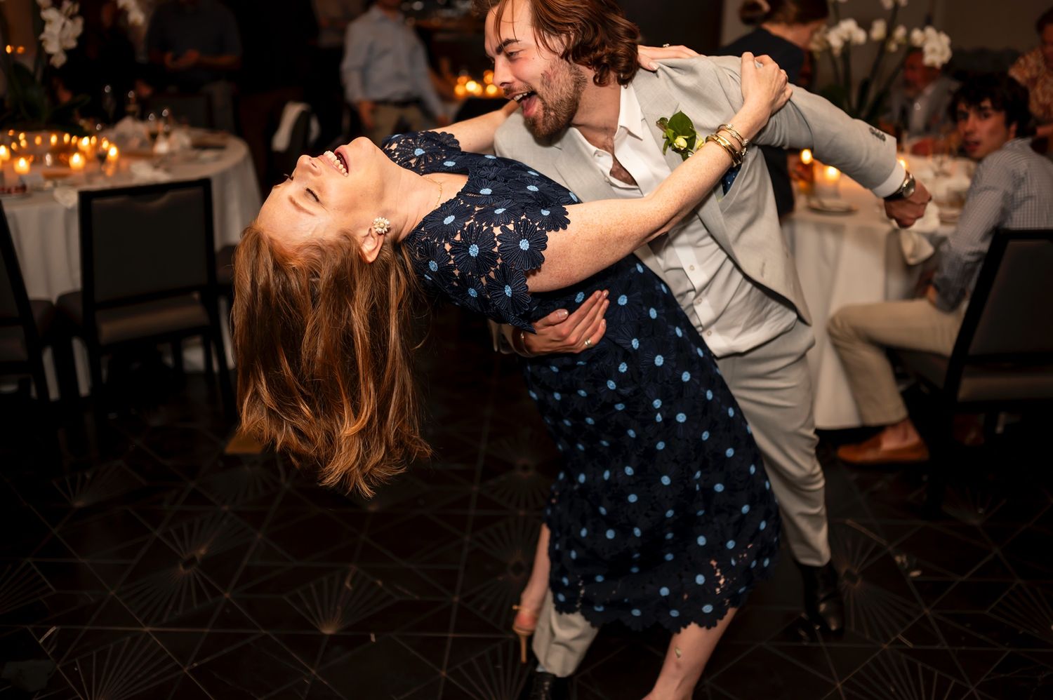 A couple dances energetically on a dark dance floor with string lights visible in the background.