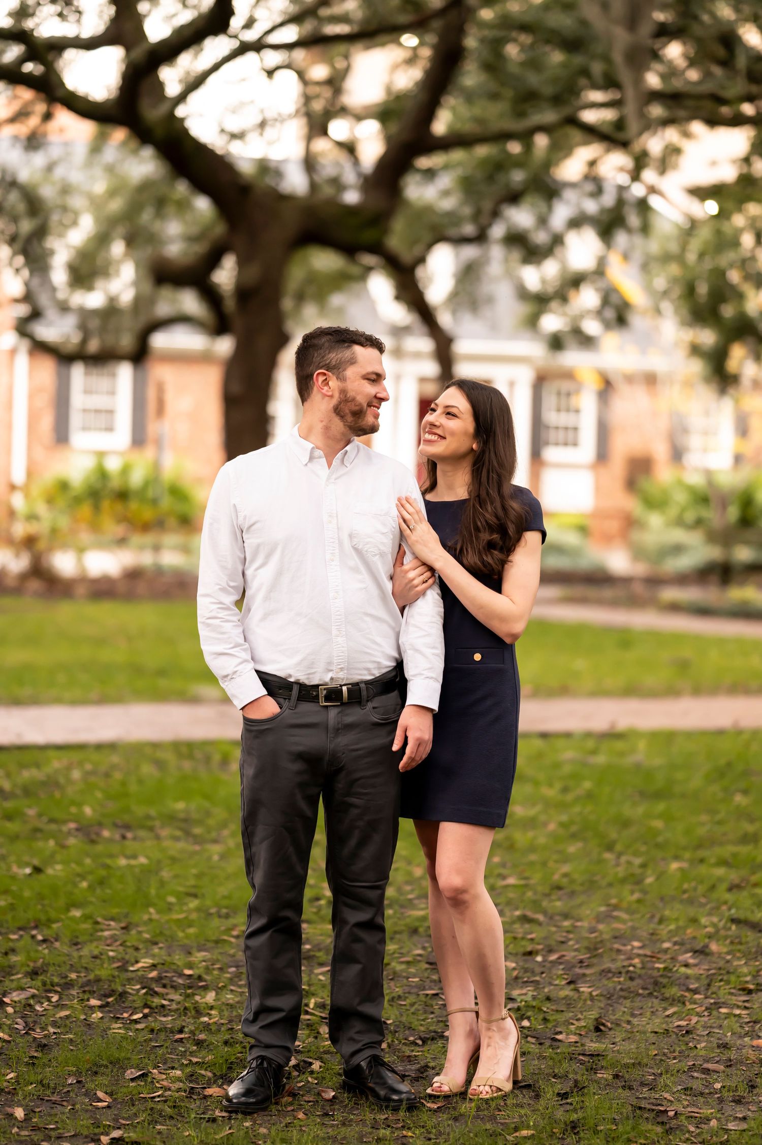 A couple poses together in a romantic outdoor engagement photo session at a park on a sunny day.